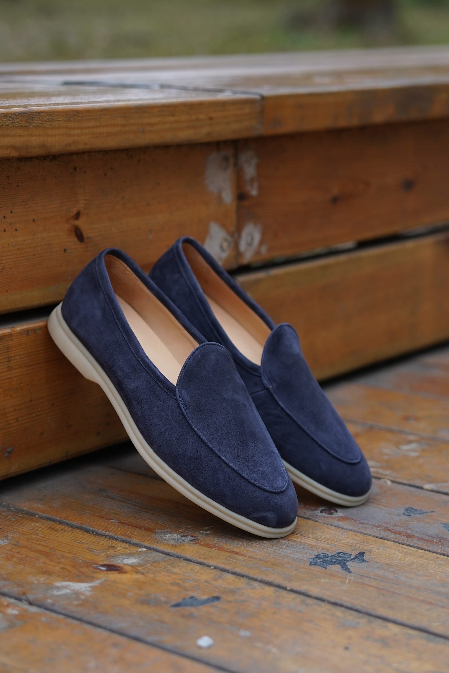 Navy blue suede Venetian loafers on a wooden surface, angled view