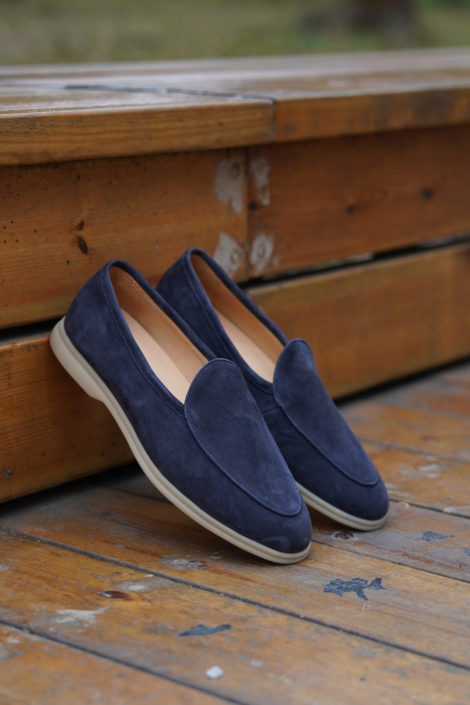 Navy blue suede Venetian loafers on a wooden surface, angled view