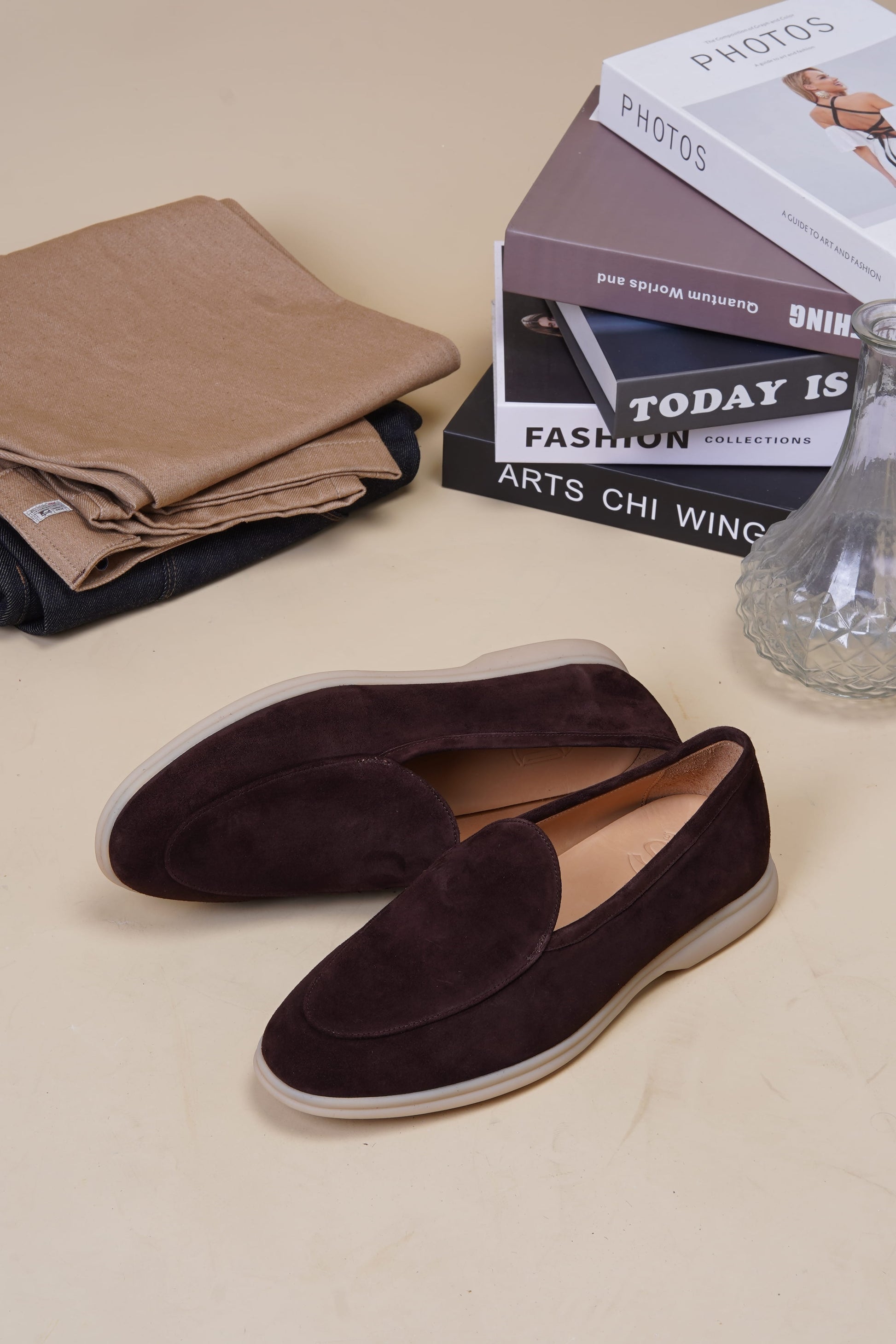 Coffee-brown suede Venetian loafers on beige surface with books, side profile
