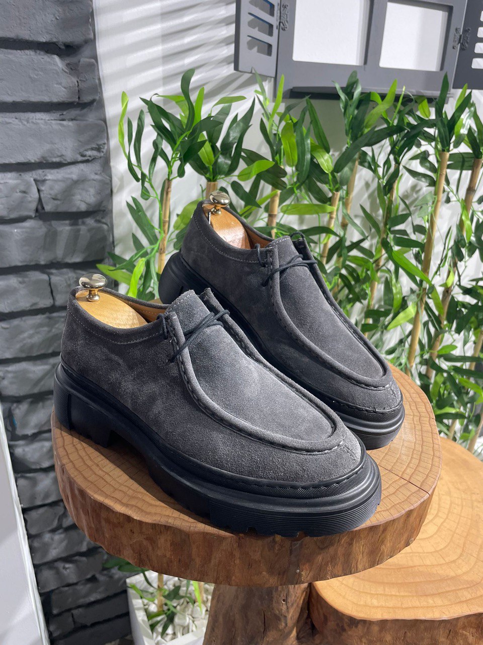 Rugged Grey Suede Lace-Up Shoes – chunky black sole, displayed on a wooden surface with green foliage, ready for urban adventure.