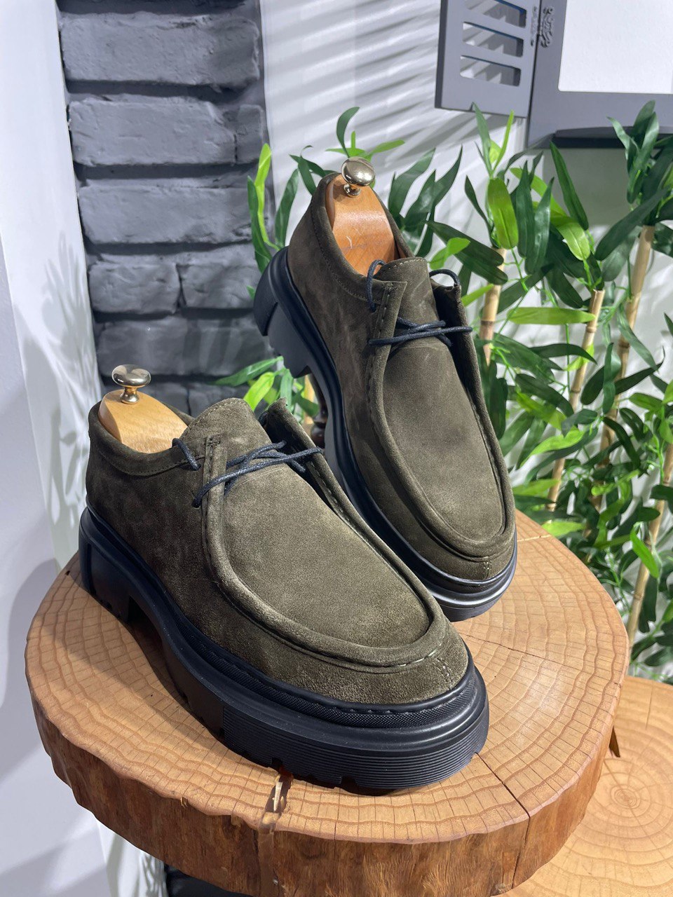 Rugged Khaki Suede Lace-Up Shoes – chunky sole and durable construction on a wooden display with brick background.