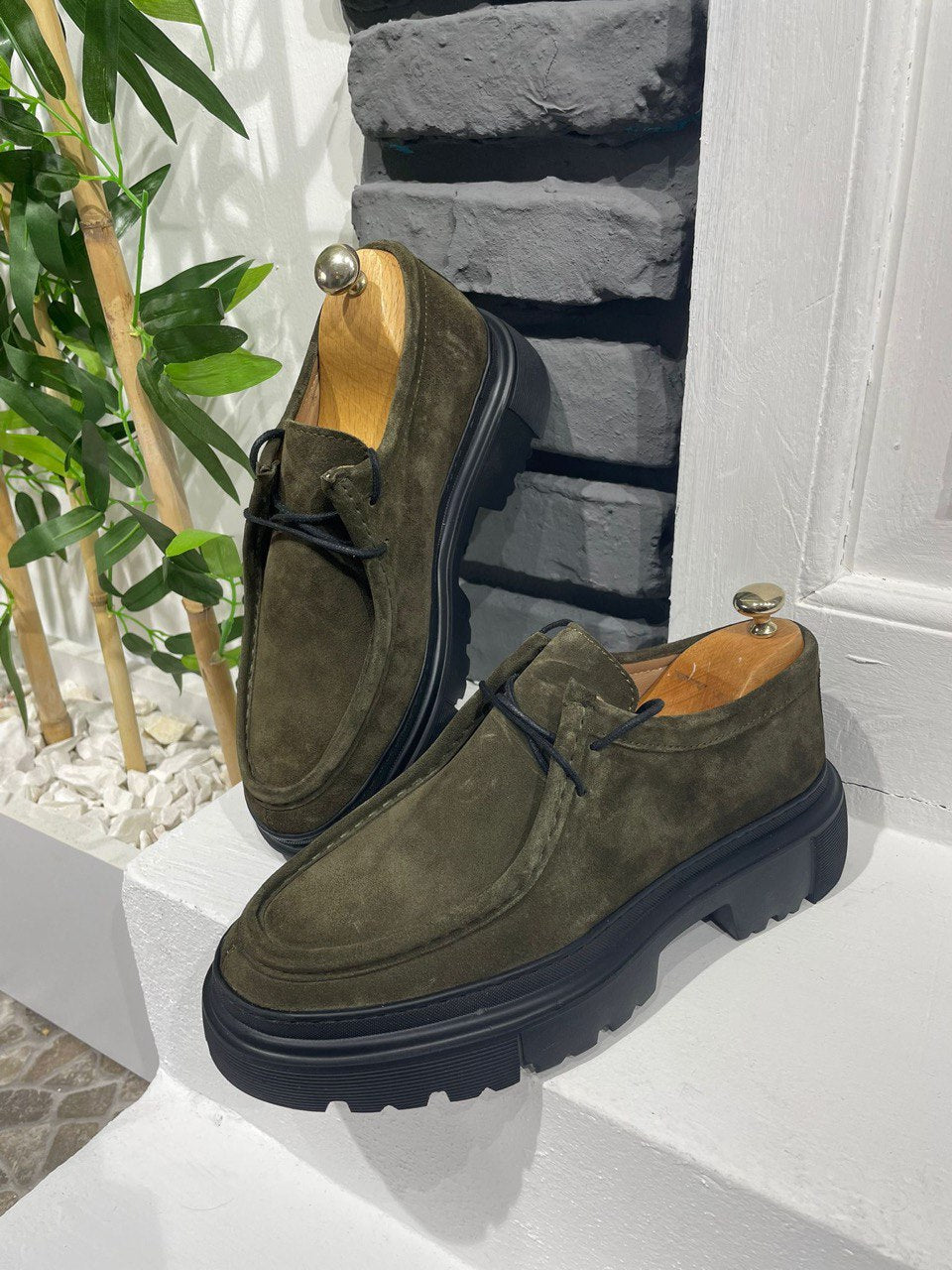 Stylish Khaki Suede Lace-Up Chunky Shoes – rugged urban footwear on a white ledge against a brick wall.