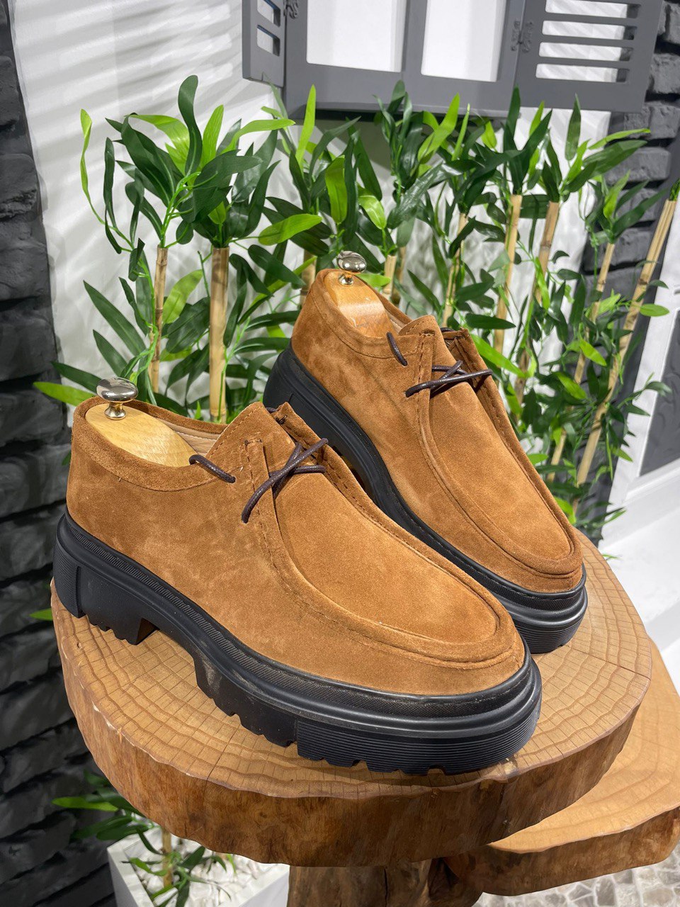 Tan Suede Lace-Up Chunky Shoes – rugged design on a wooden display with green plants, ideal for traction and support.