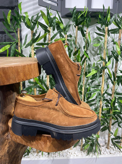 Rugged Tan Suede Lace-Up Shoes – chunky black sole, displayed on a wooden surface with green foliage, ready for urban adventure.