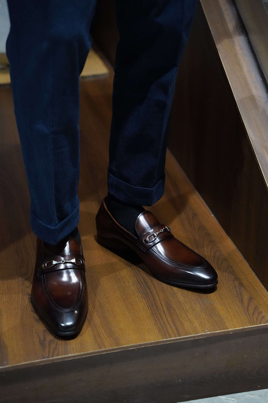 Sophisticated Brown Leather Bit Loafers For Men – worn by a man in navy trousers, standing on wooden steps, emphasizing sleek silhouette and distinctive metal buckle.