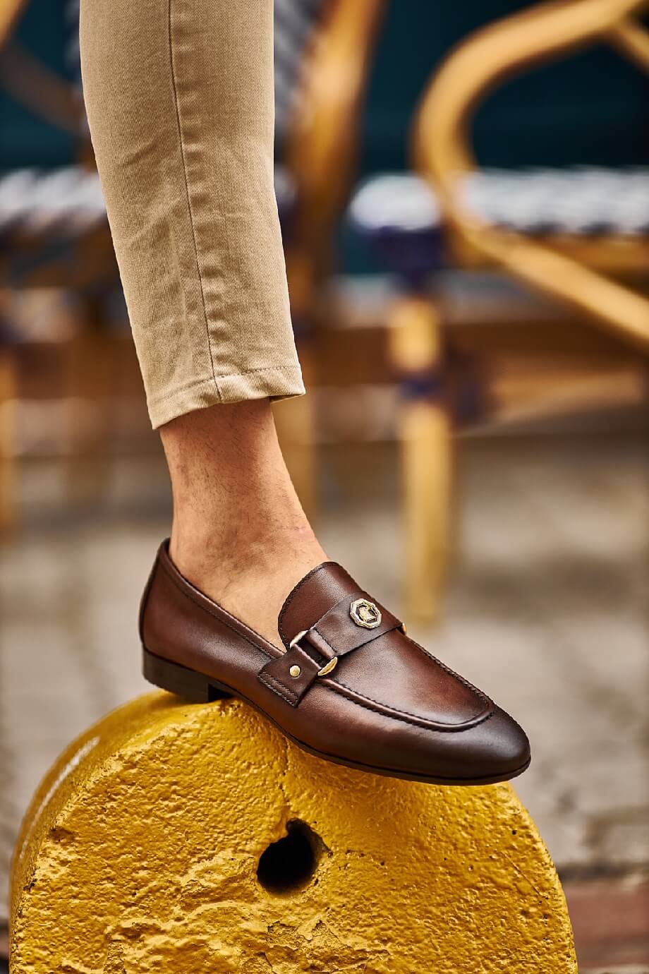 Sophisticated Brown Leather Penny Loafers for Business & Casual Wear – worn by a man in tan chinos, sitting on a chair with one foot raised, highlighting the elegant horsebit and comfort.