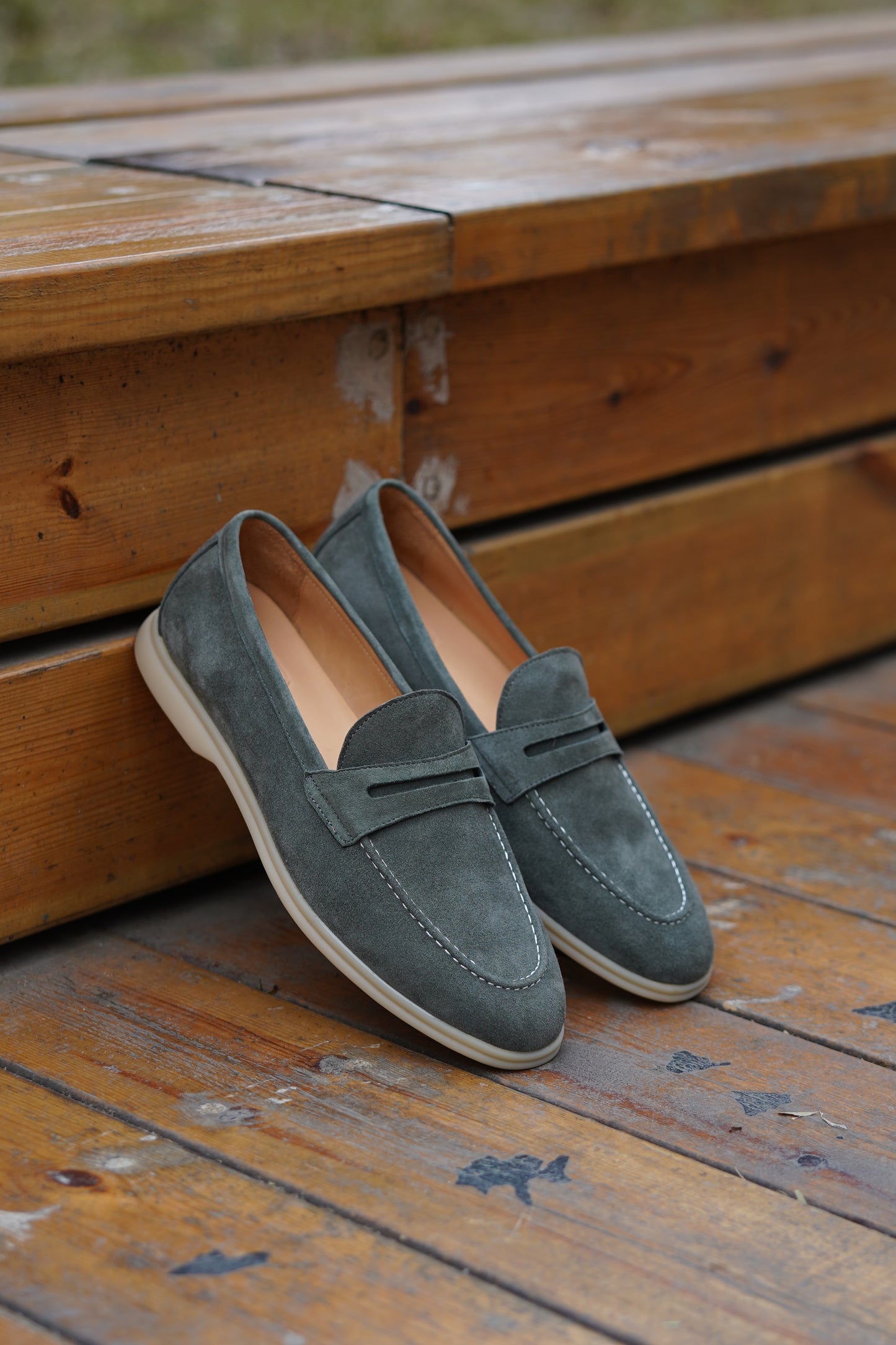 Pale cyan suede penny loafers on a wooden surface, angled view