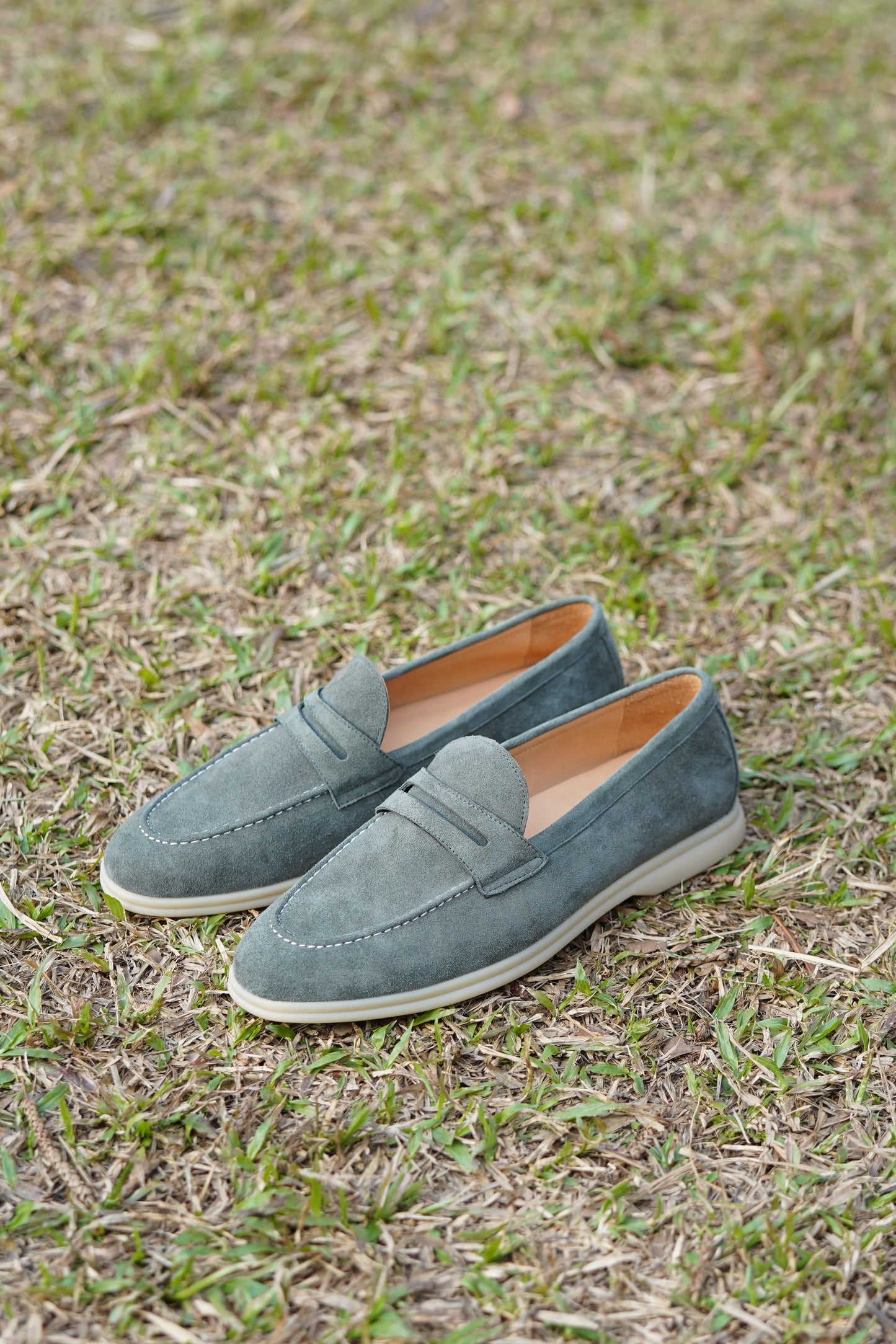 Pale cyan suede penny loafers outdoors on grass, side view