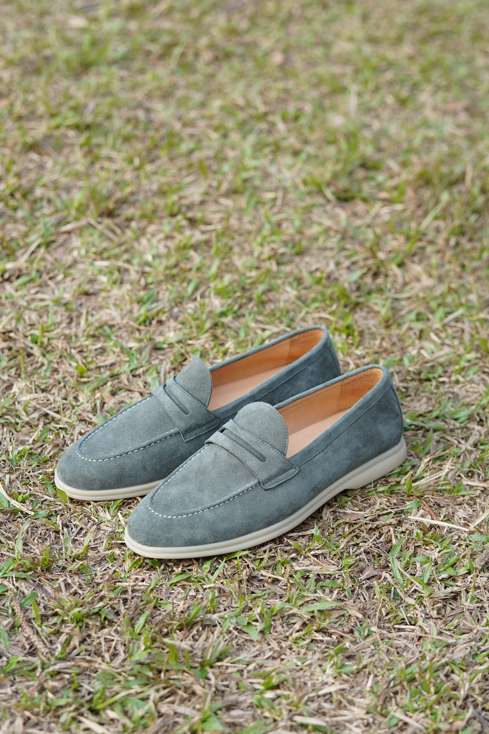 Pale cyan suede penny loafers outdoors on grass, side view