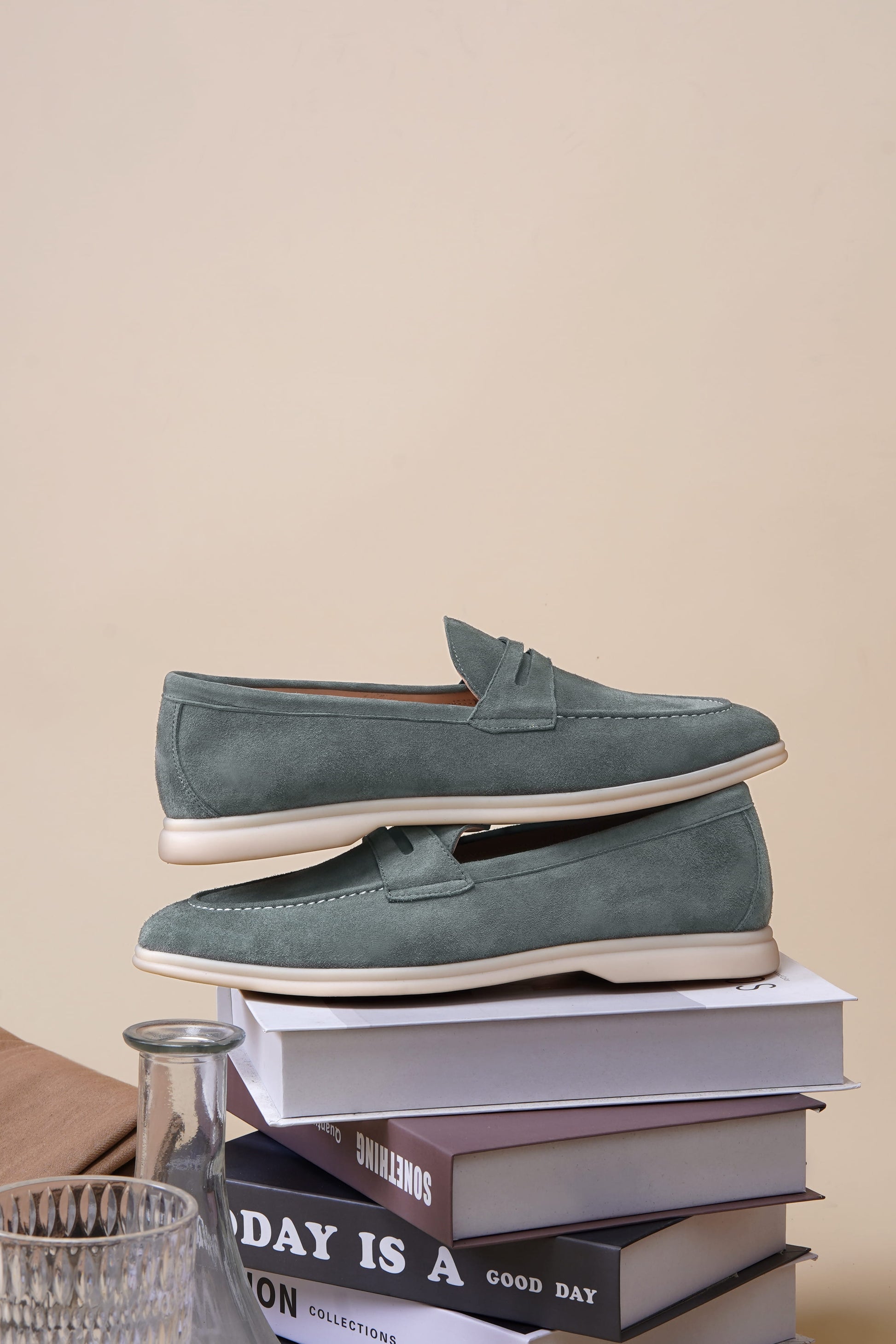 Pale cyan suede penny loafers on a stack of books, styled view