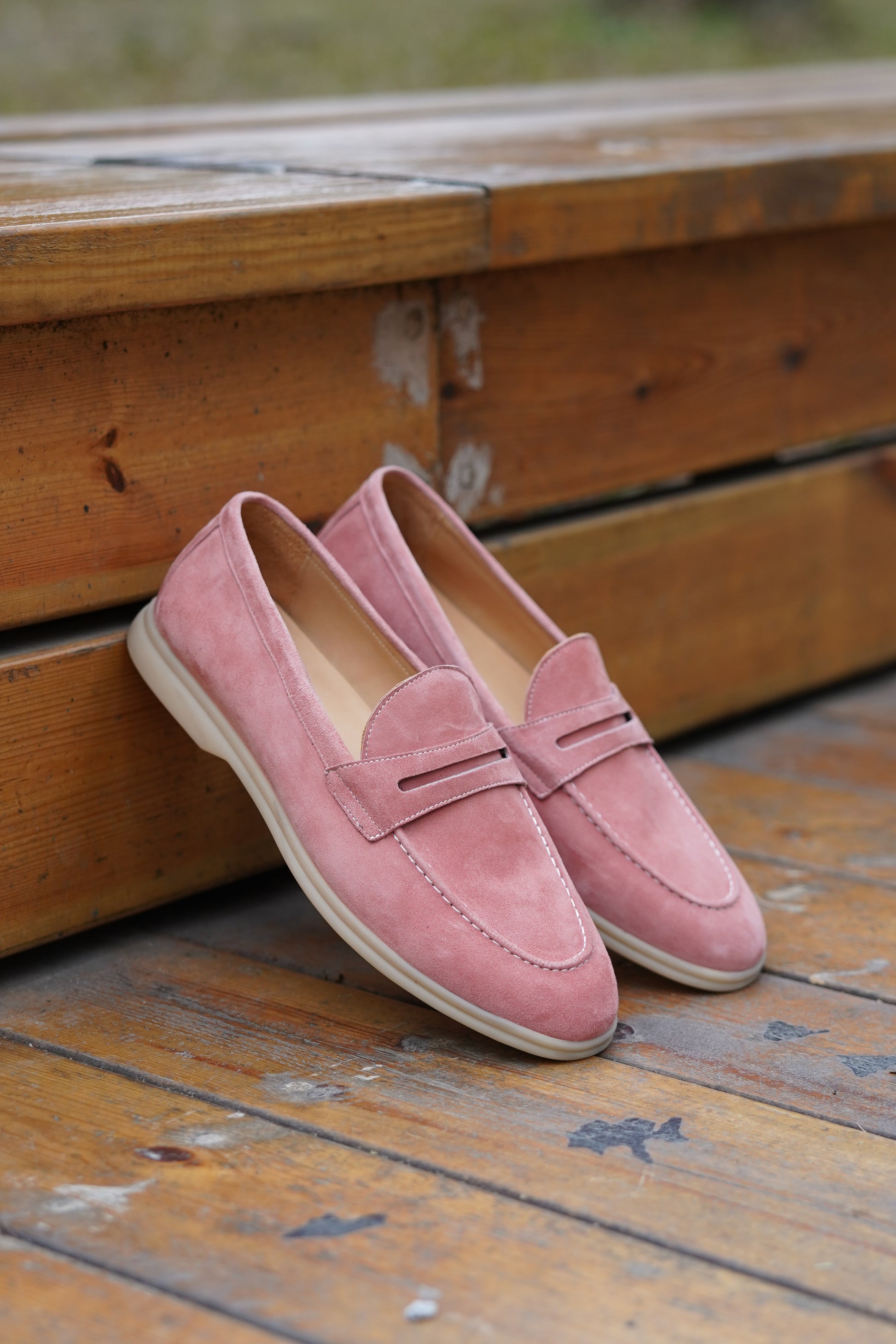 Pair of pink suede penny loafers on a wooden surface, side view