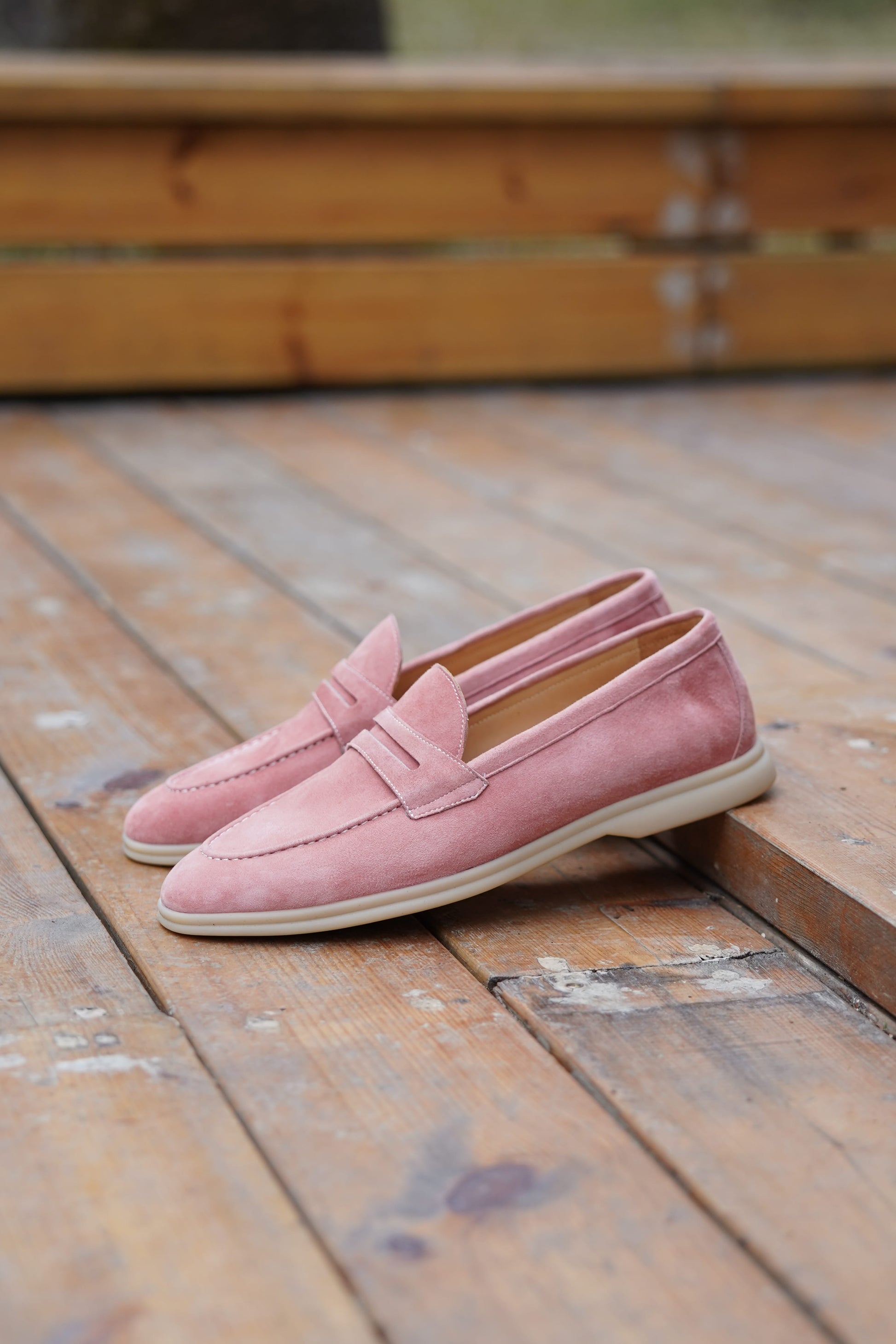 Pink suede penny loafers on a wooden surface, angled view