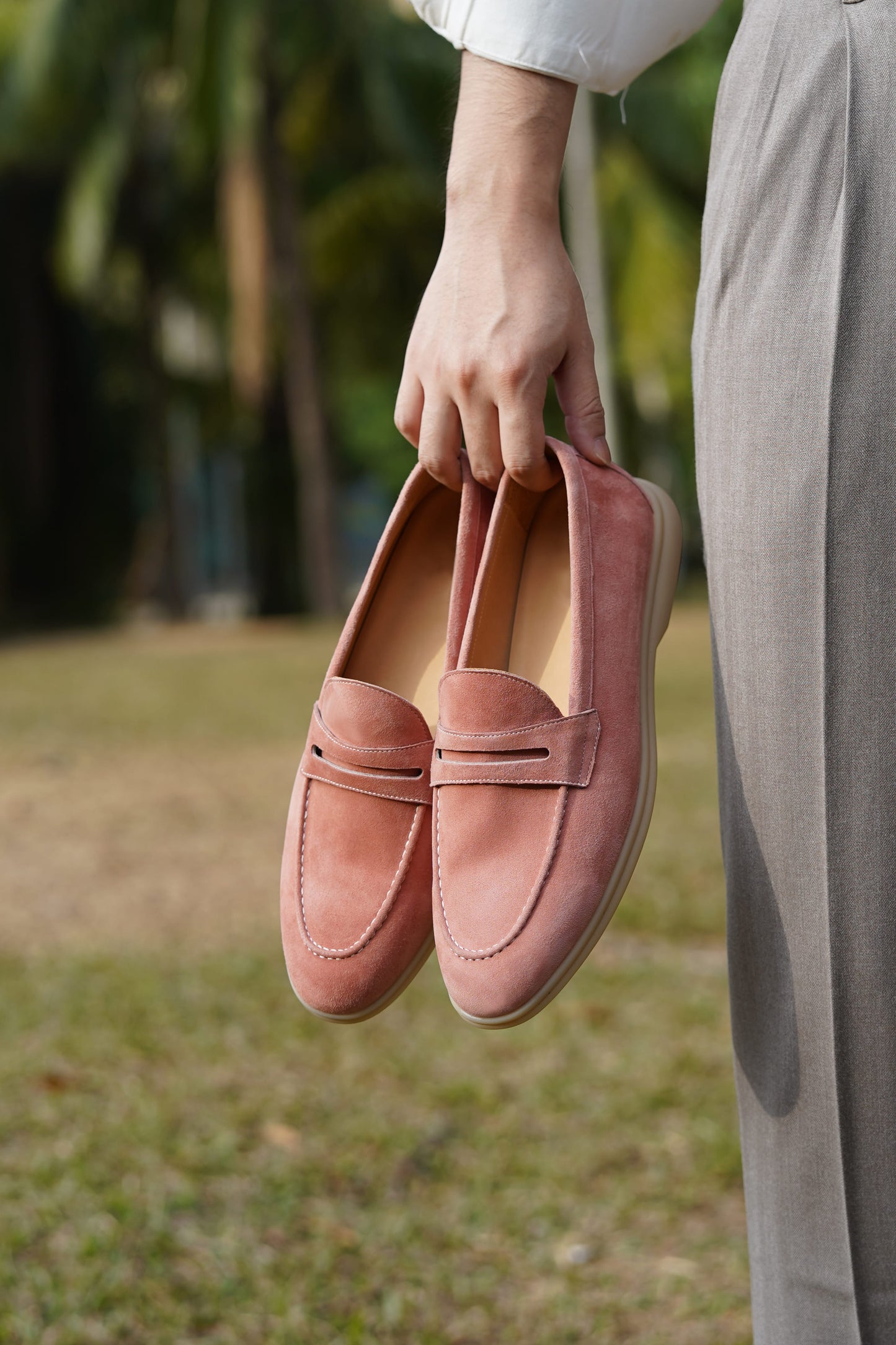 Hand holding Monaco pink suede penny loafers outdoors, three-quarter view