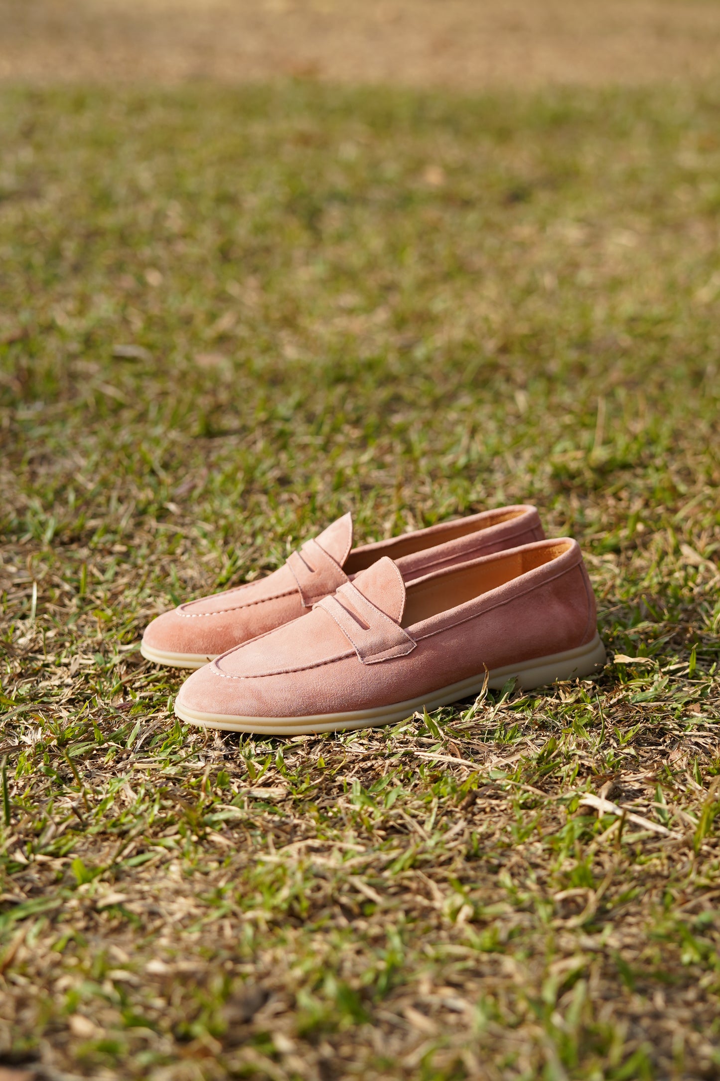Pink suede penny loafers outdoors on grass, side view