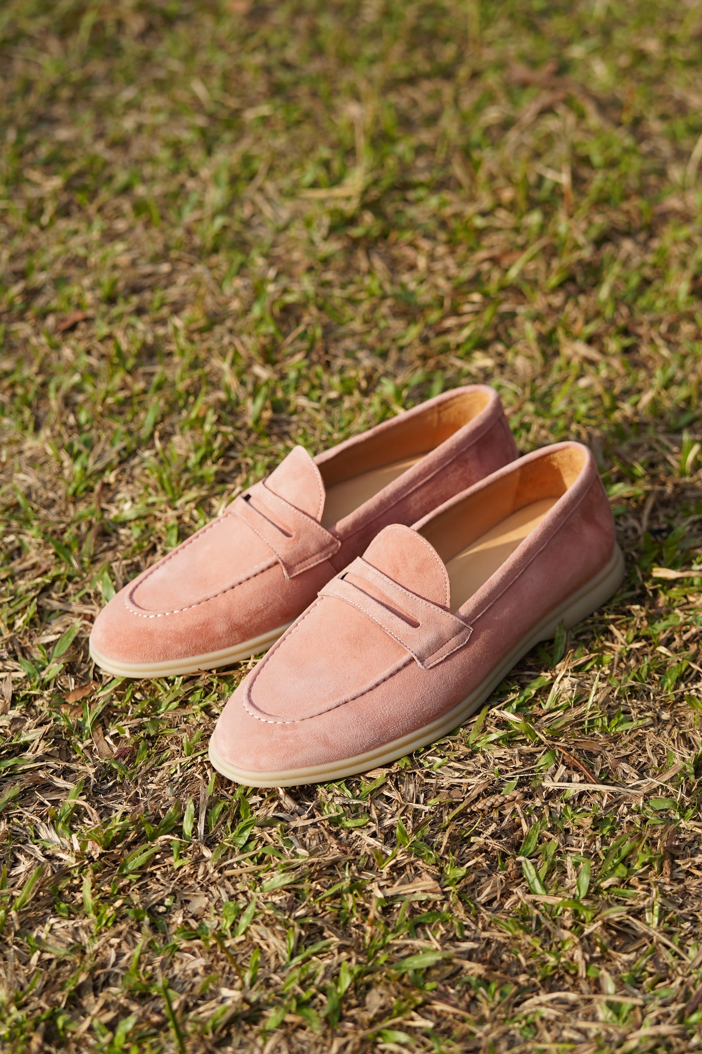 Pair of pink suede penny loafers on beige background, top view