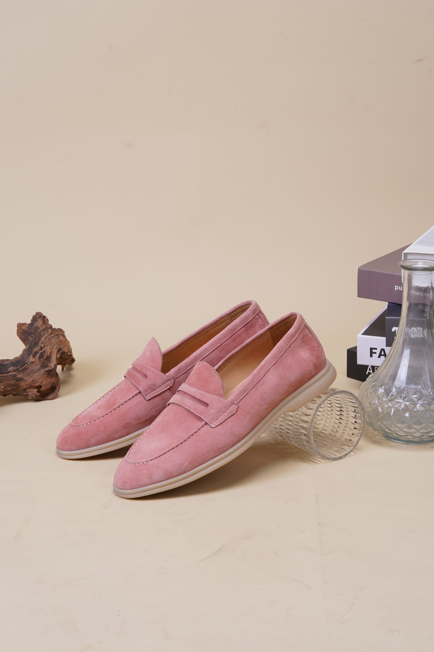 Pink suede penny loafers on neutral surface, side profile
