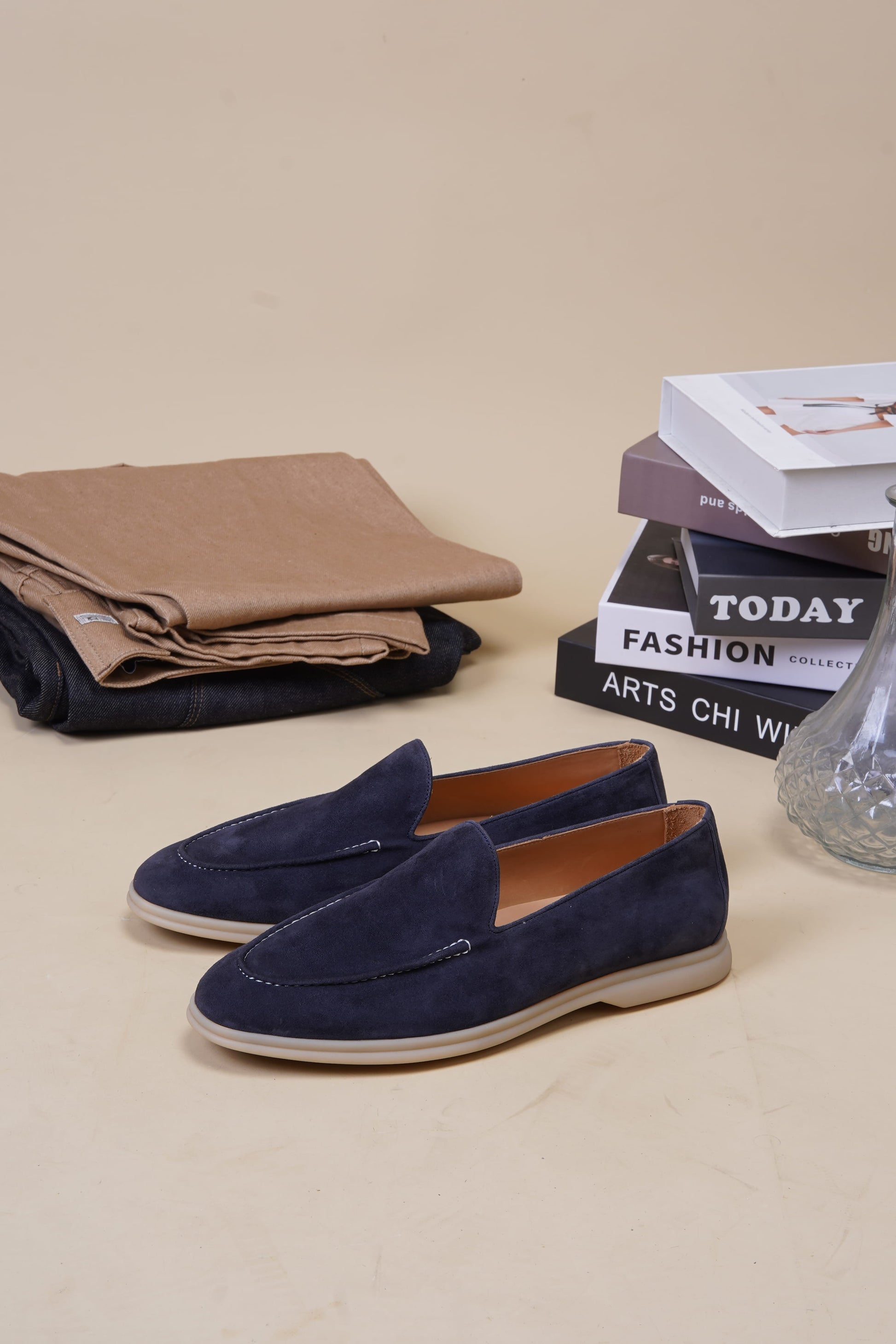 Deep navy suede penny loafers on beige surface with folded fabric and books, angled pair