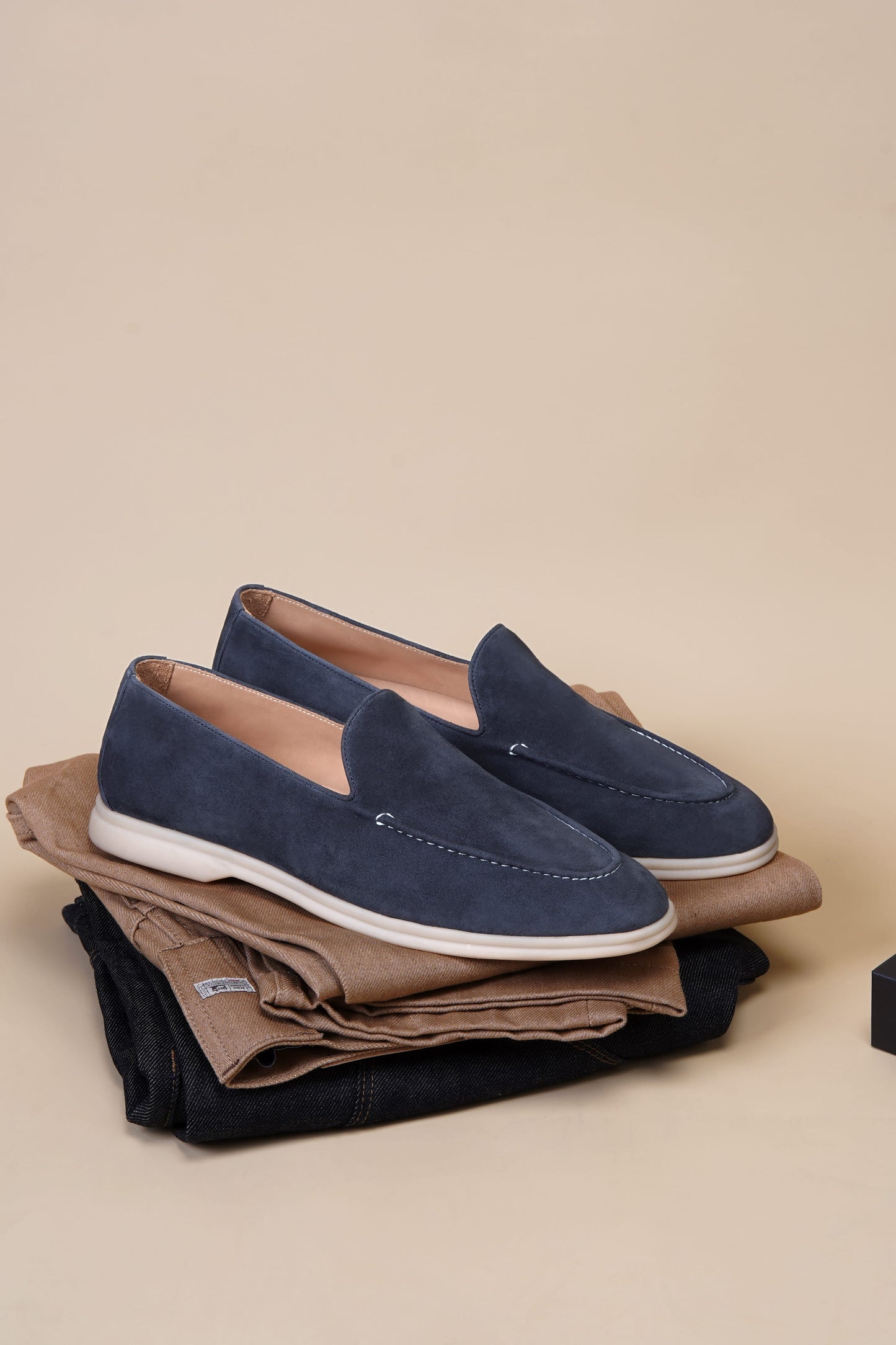 Deep navy suede penny loafers on folded clothes, styled view