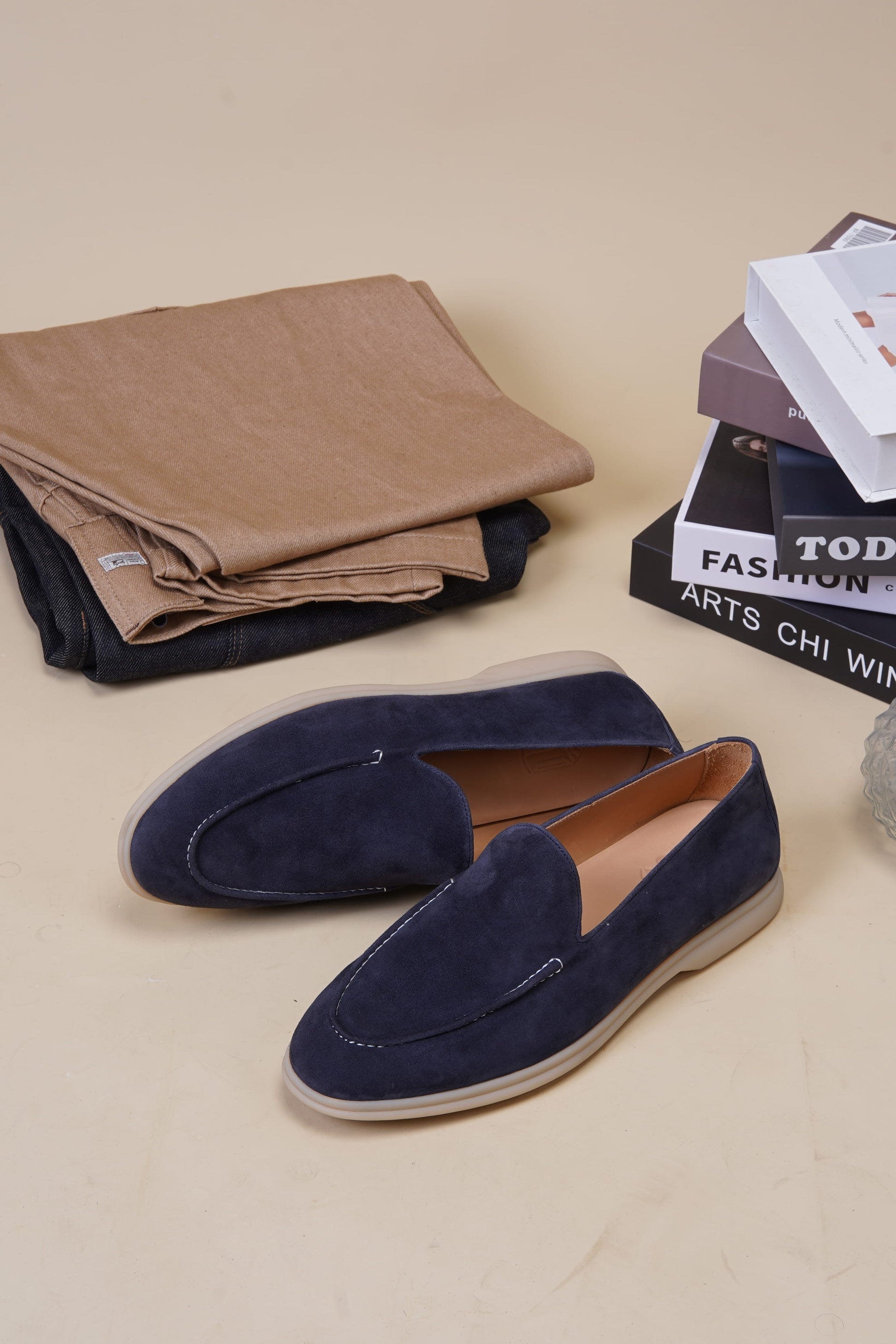 Deep navy suede penny loafers on beige surface with magazines, side profile