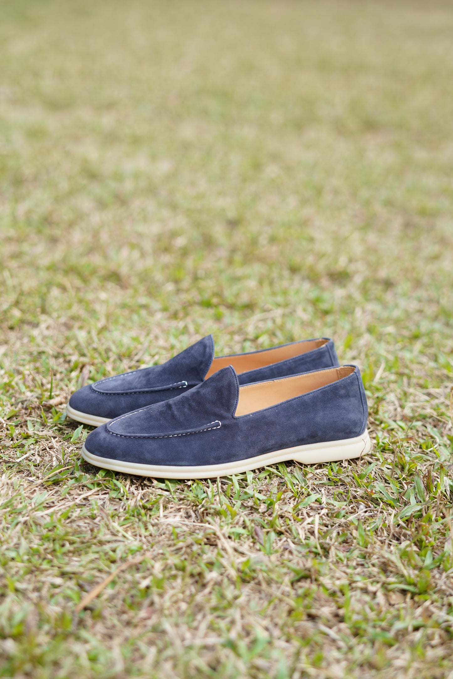 Pair of deep navy suede penny loafers on grass, outdoor view