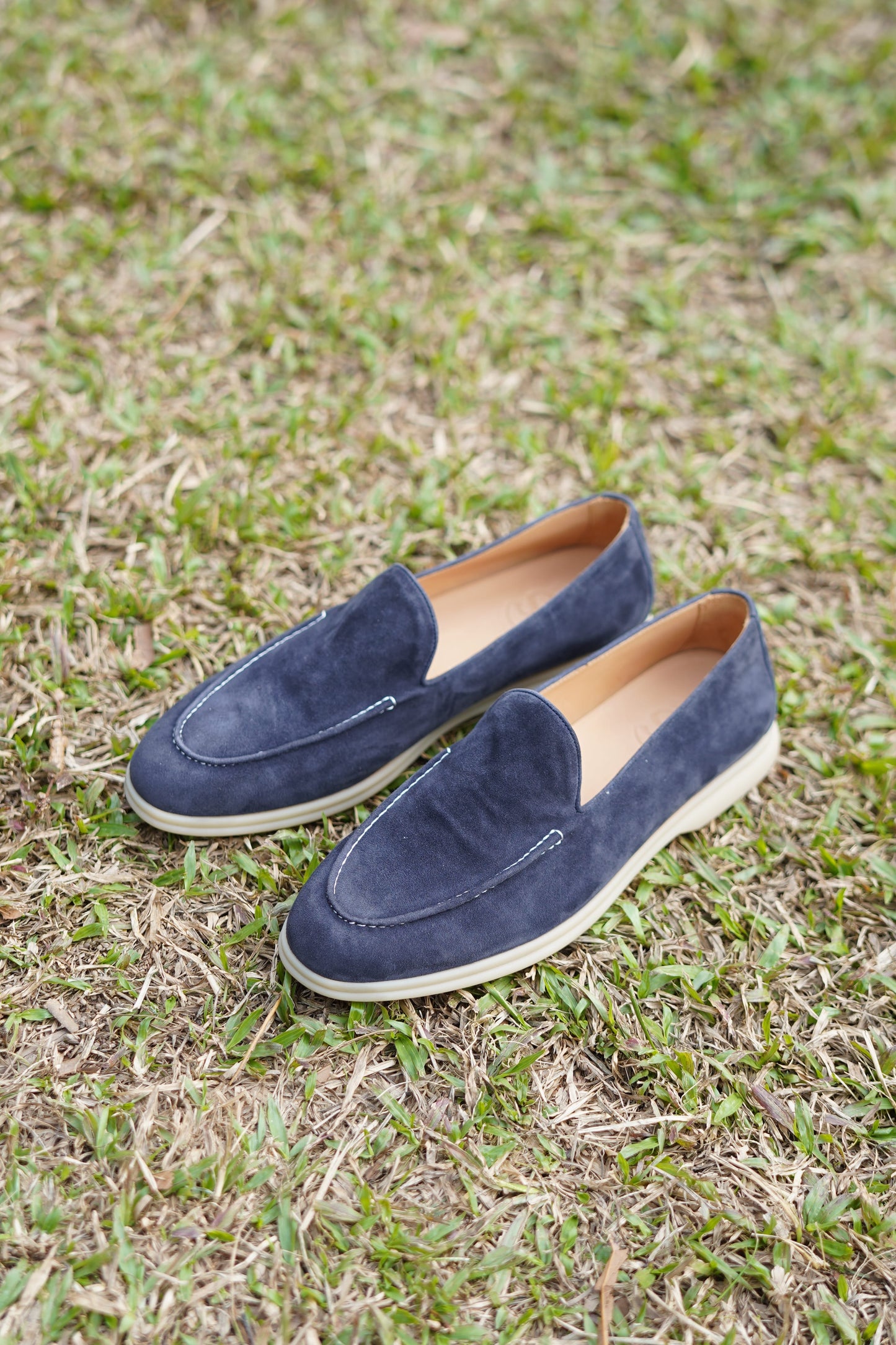 Pair of deep navy suede penny loafers on grassy background, side view