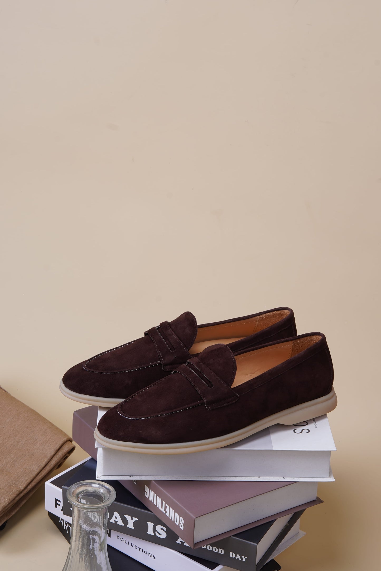 Espresso-brown suede penny loafers on a stack of books, styled view