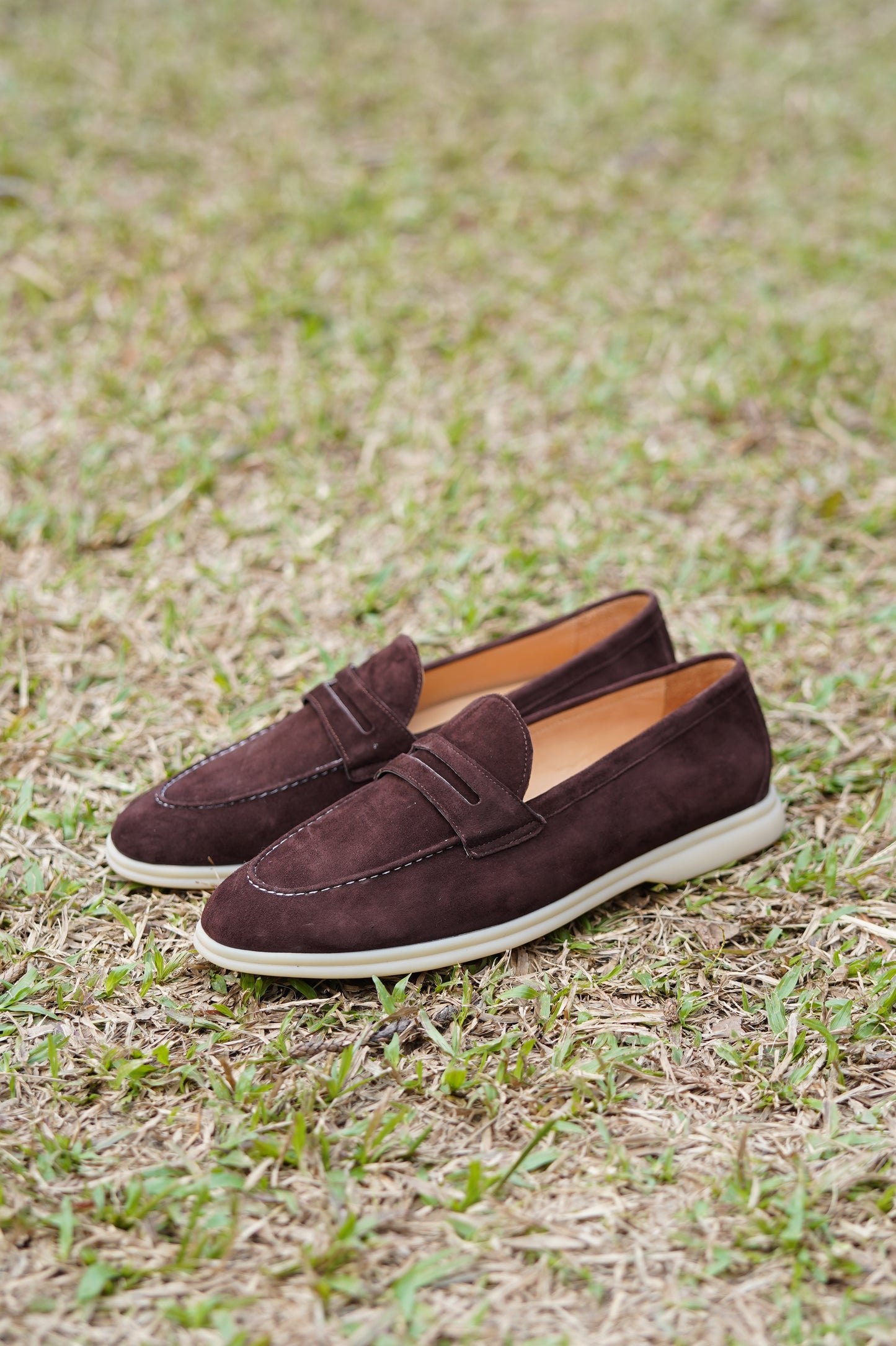 Pair of espresso-brown suede penny loafers on grass, outdoor side view