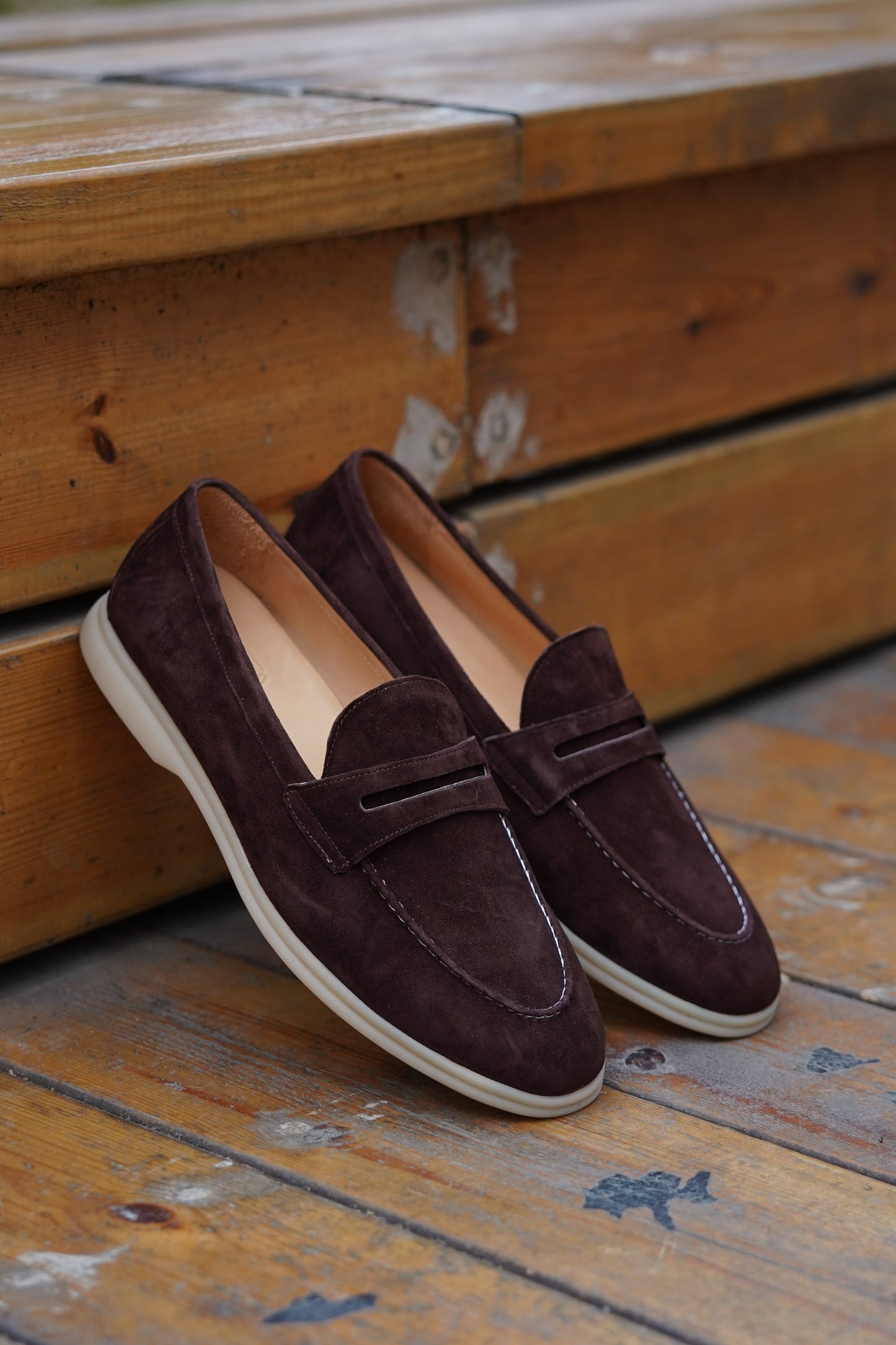 Espresso-brown suede penny loafers on a wooden surface, side view