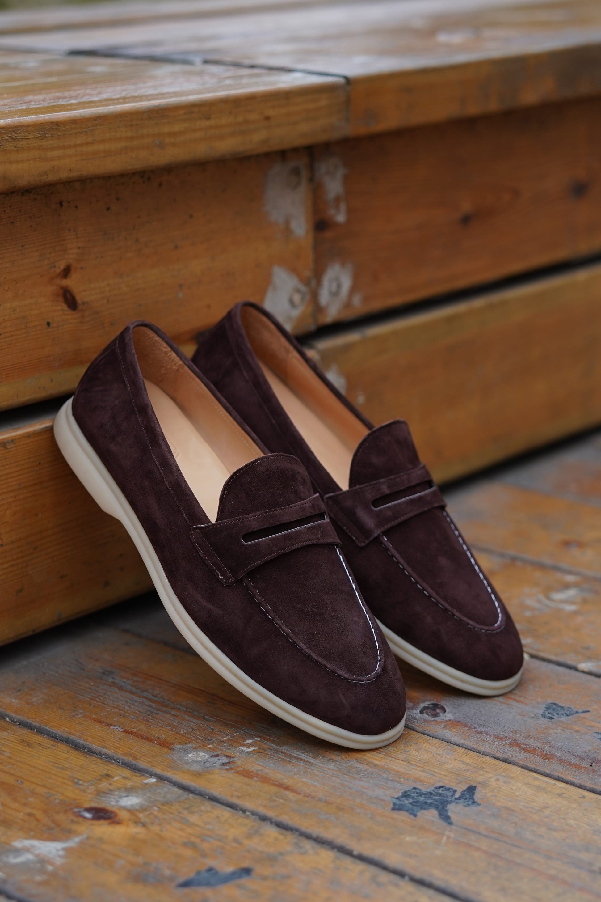 Espresso-brown suede penny loafers on a wooden surface, side view