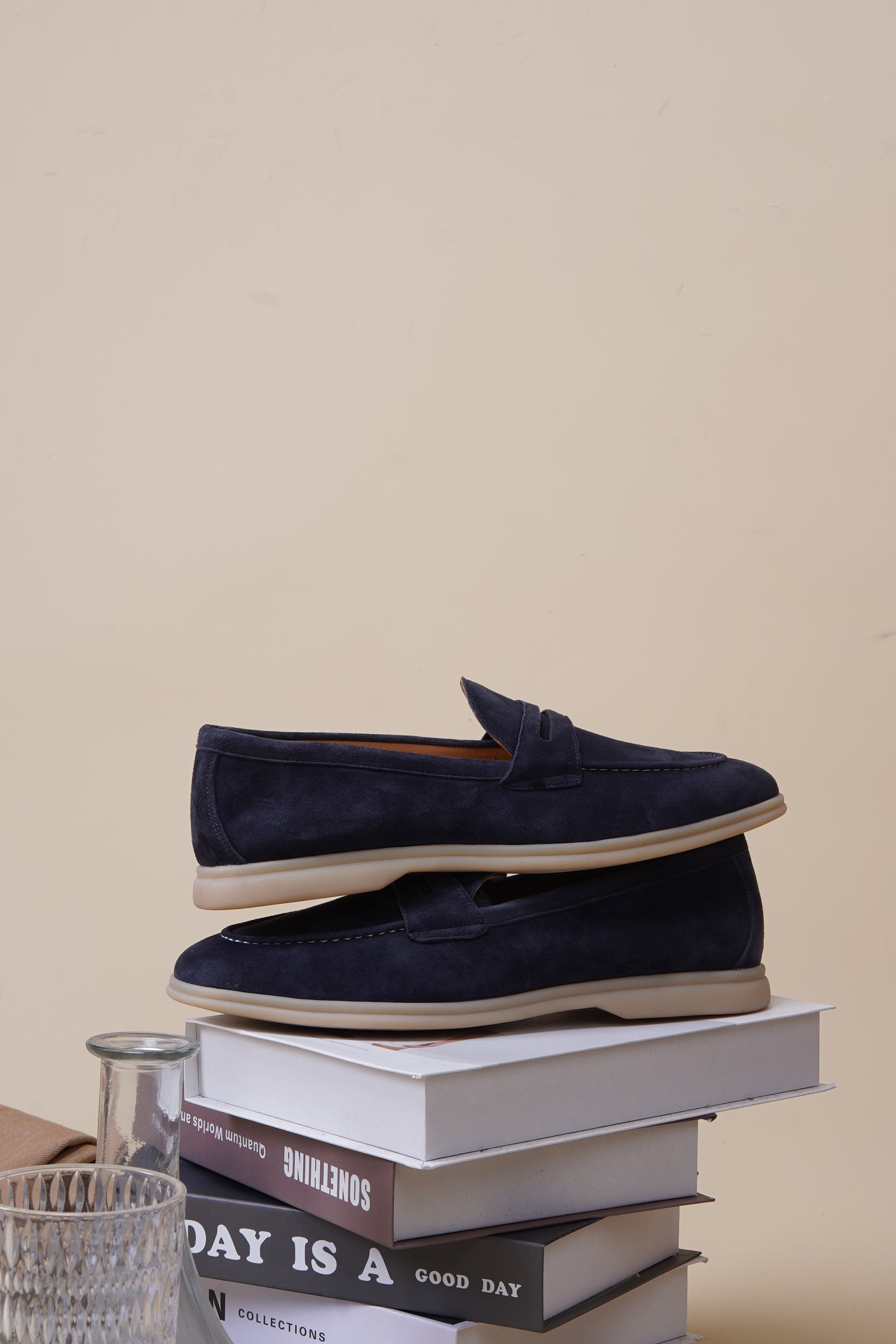 Pair of navy blue suede penny loafers on neutral surface, side profile