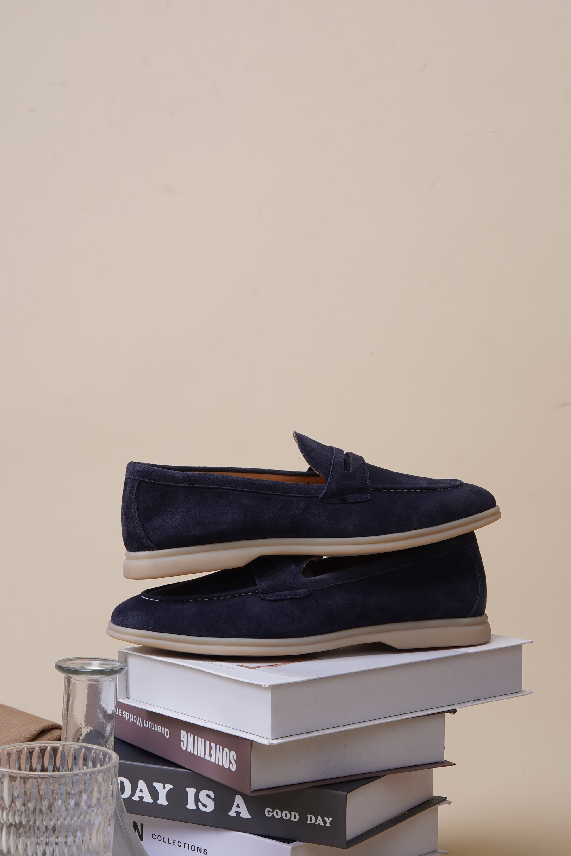 Pair of navy blue suede penny loafers on neutral surface, side profile
