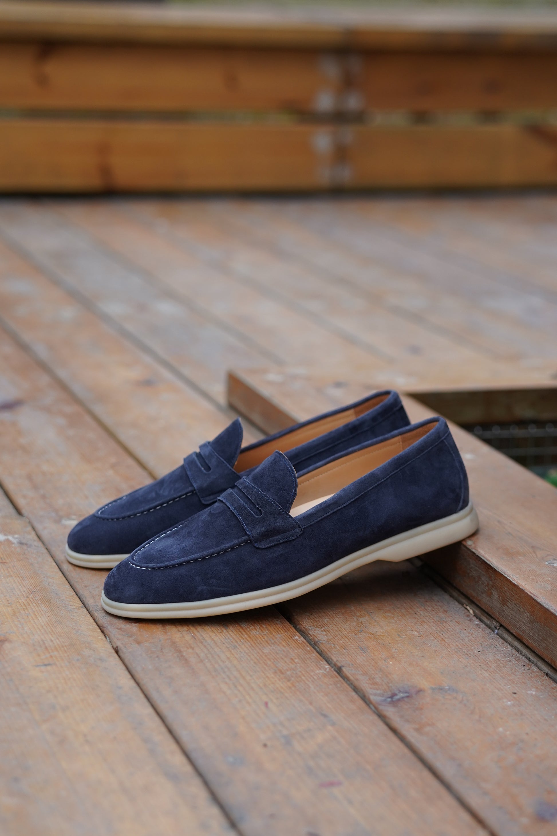 Navy blue suede penny loafers outdoors, three-quarter view