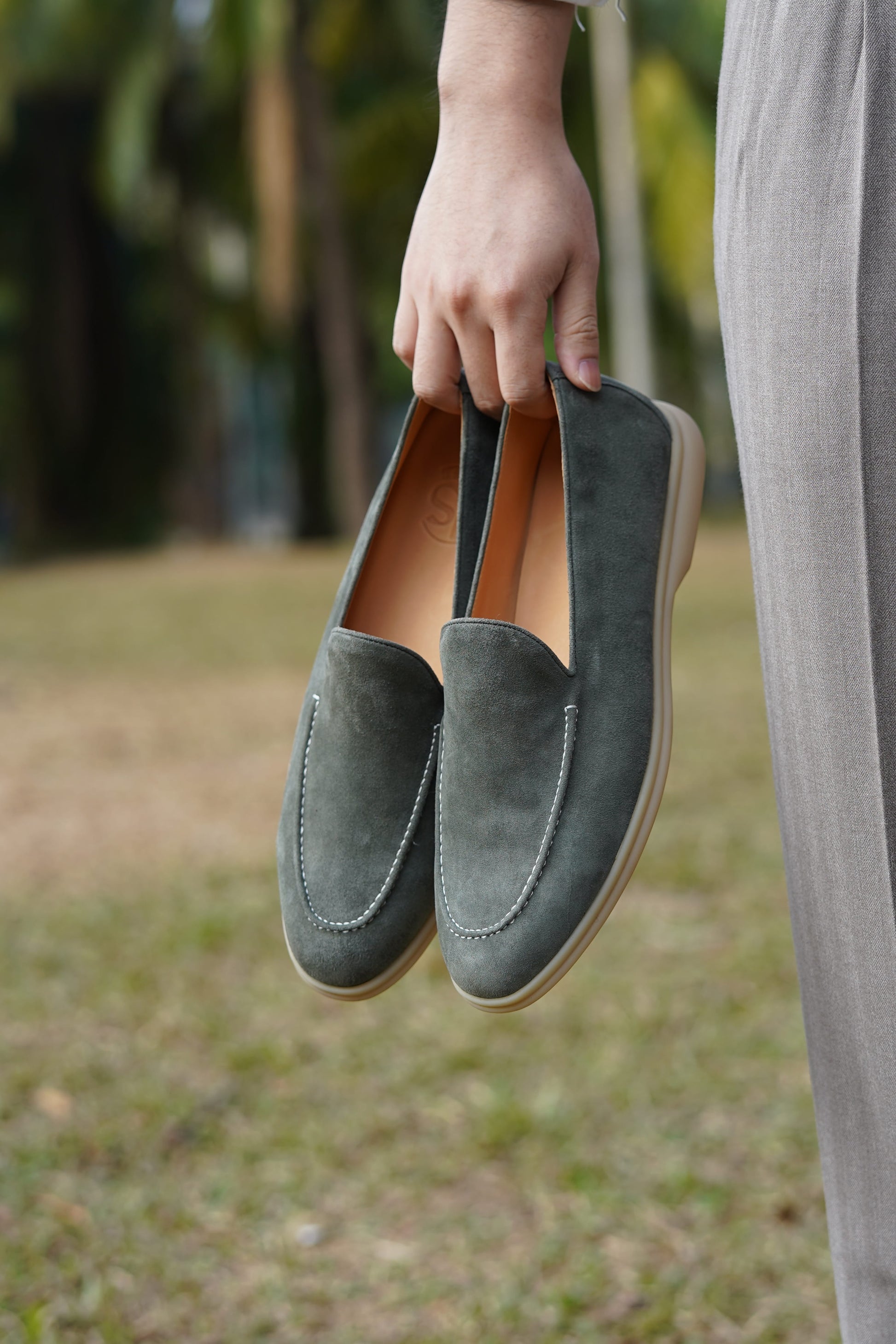 Hand holding Tuscany sage gray suede Venetian loafers outdoors, three-quarter view