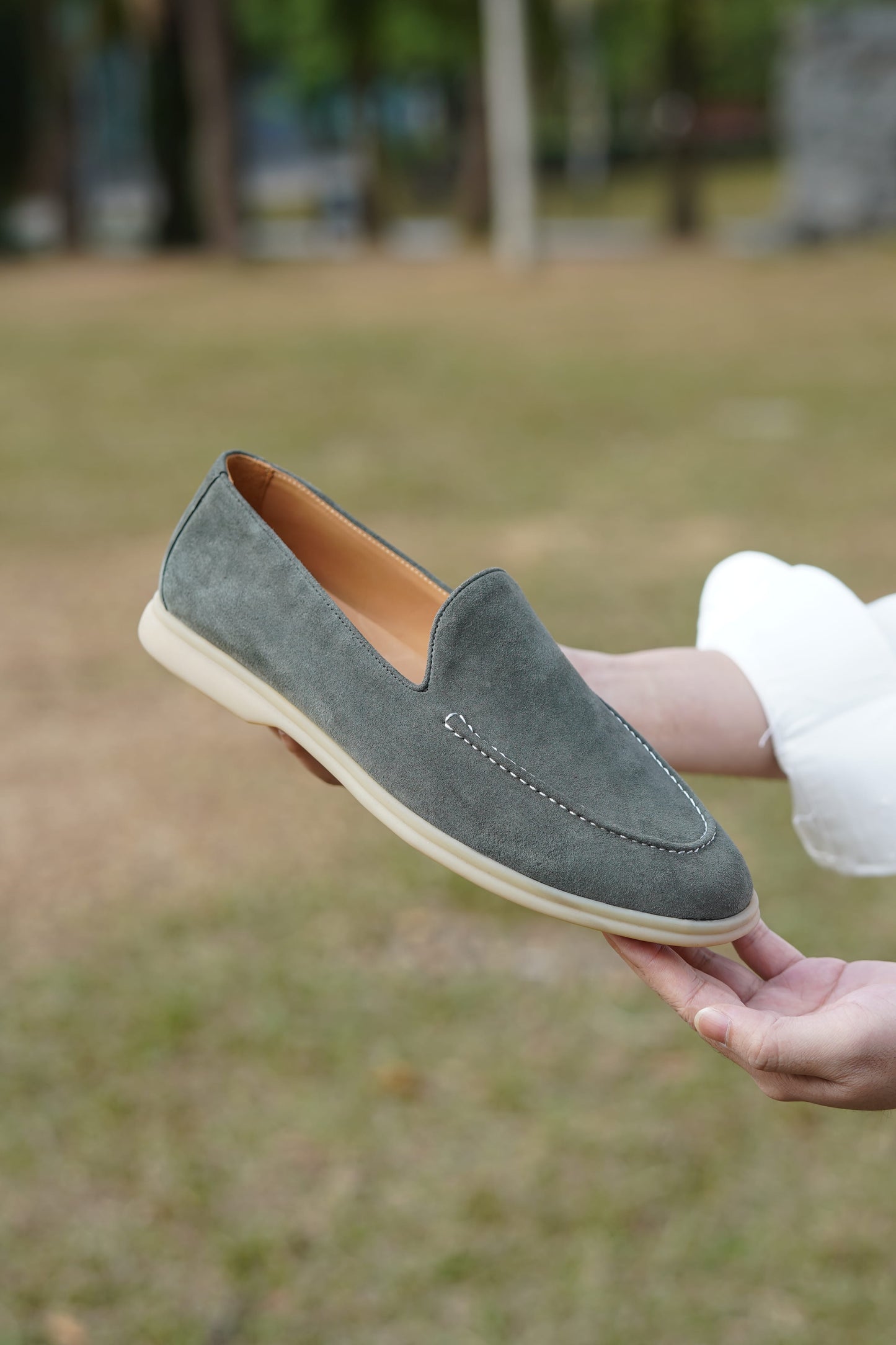 Man holding a sage gray suede Venetian loafer outdoors, close detail