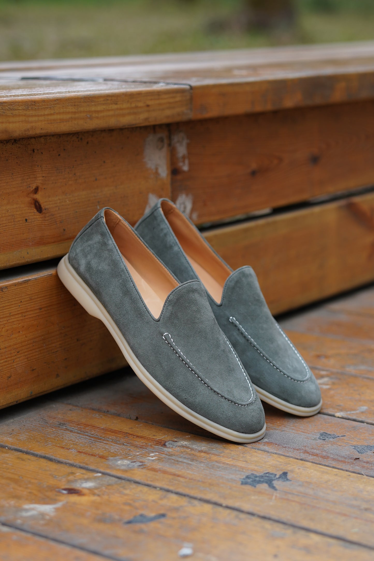 Pair of sage gray suede Venetian loafers on a wooden surface, angled view