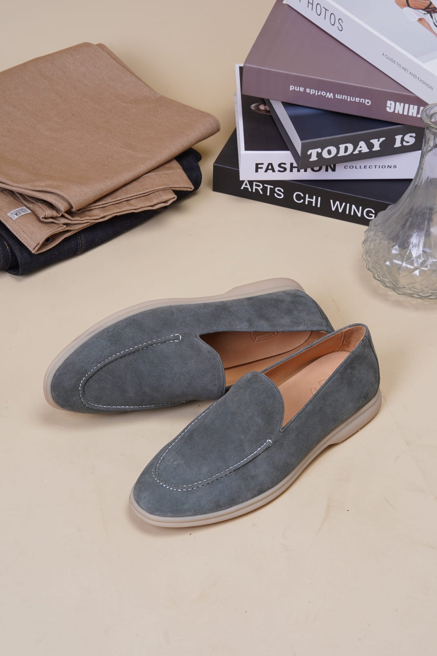 Sage gray suede Venetian loafers on beige surface with folded fabric and magazine, side profile