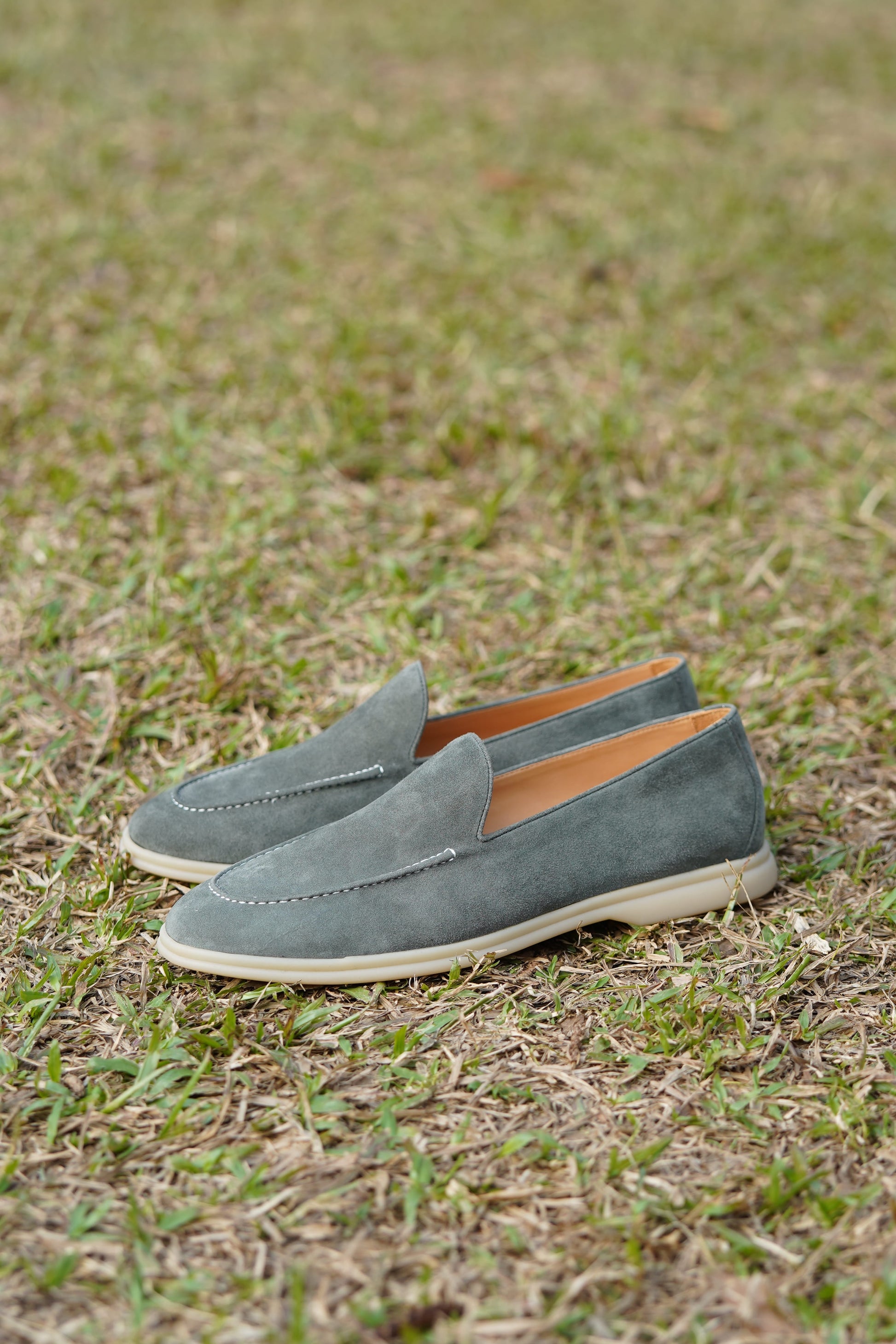 Sage gray suede Venetian loafers on a grassy surface, side view