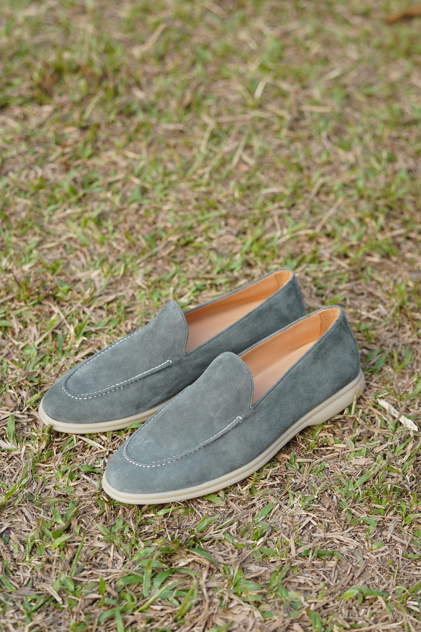 Pair of sage gray suede Venetian loafers on grass, outdoor view