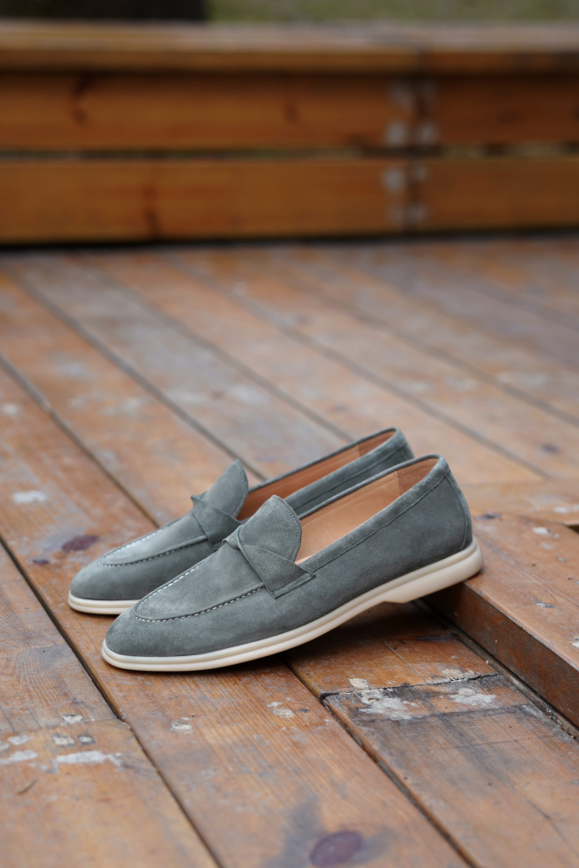Hand holding green suede twist-strap loafers outdoors, three-quarter view