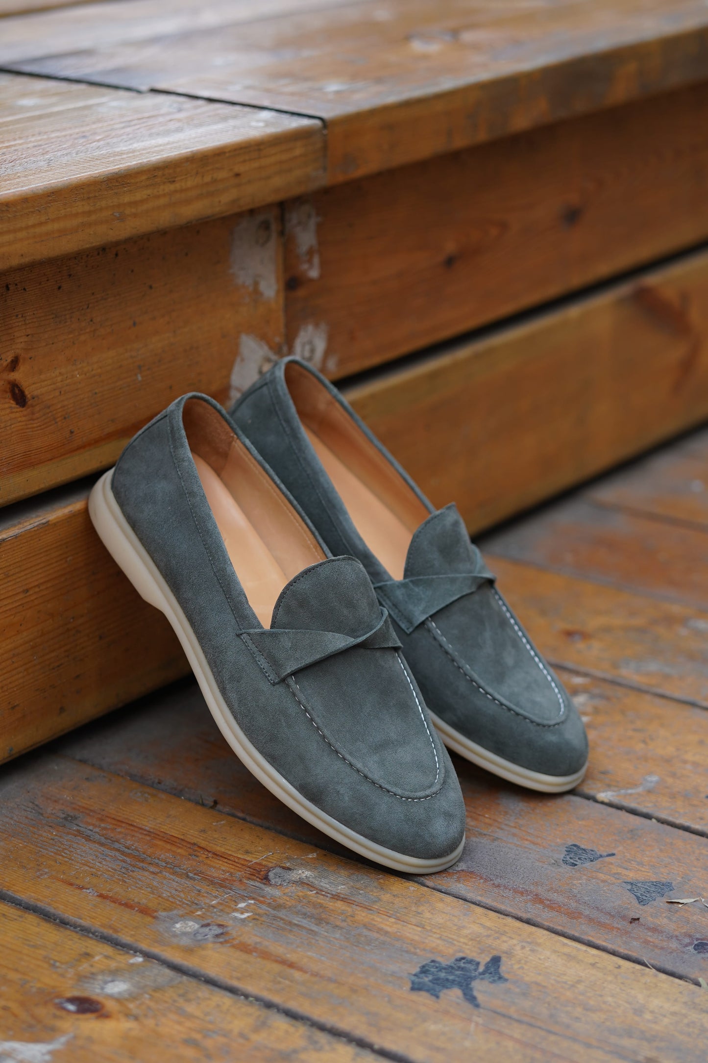 Pair of green suede twist-strap loafers on neutral surface, side profile