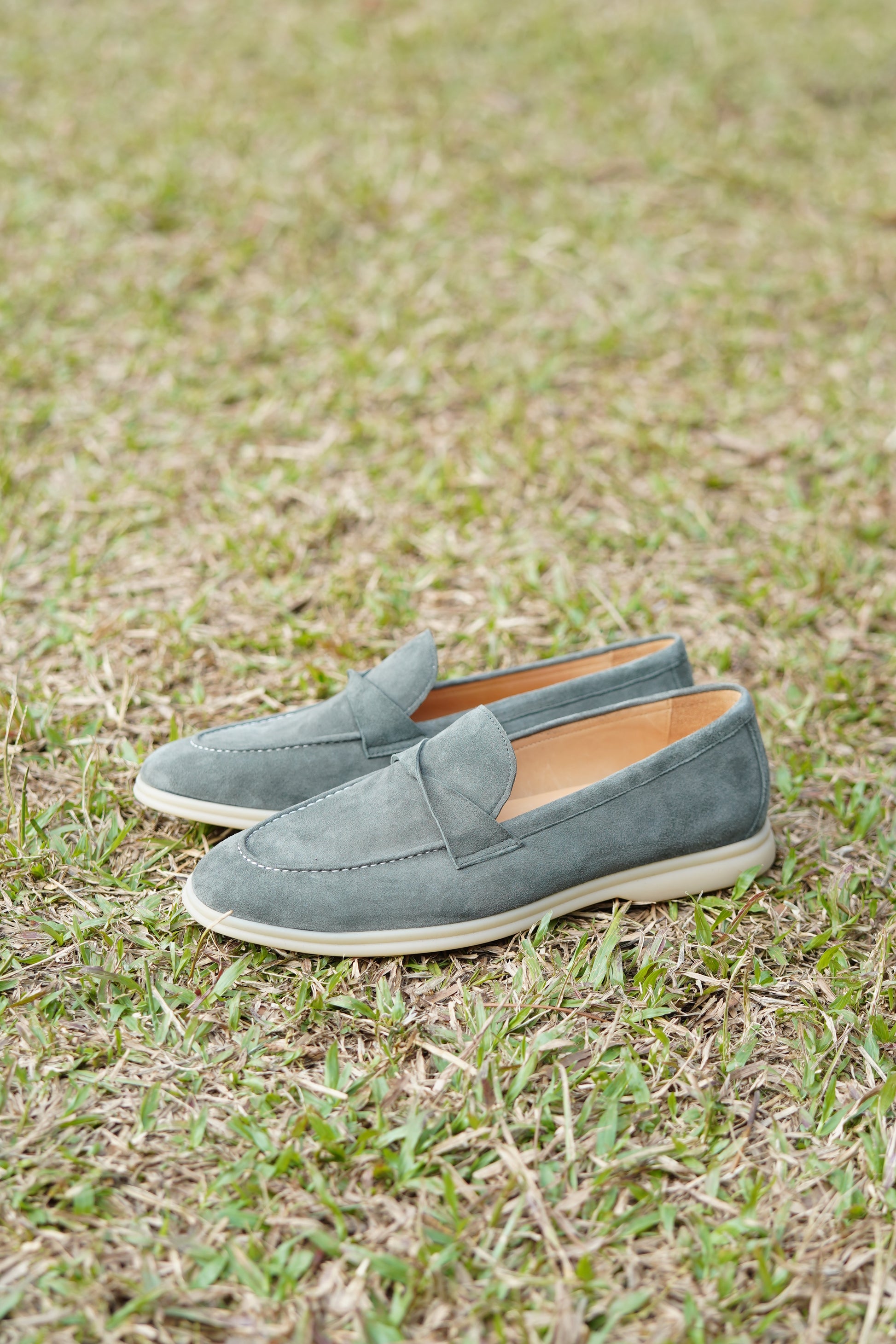 Green suede twist-strap loafers on a wooden surface, angled view