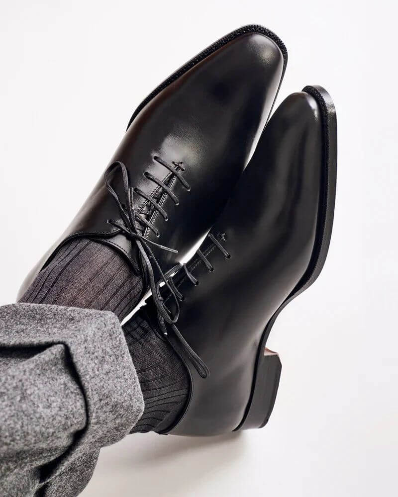 The Nero Noir Polished Black Wholecut Oxfords worn with grey trousers – top angled view showcasing closed lacing and sleek silhouette