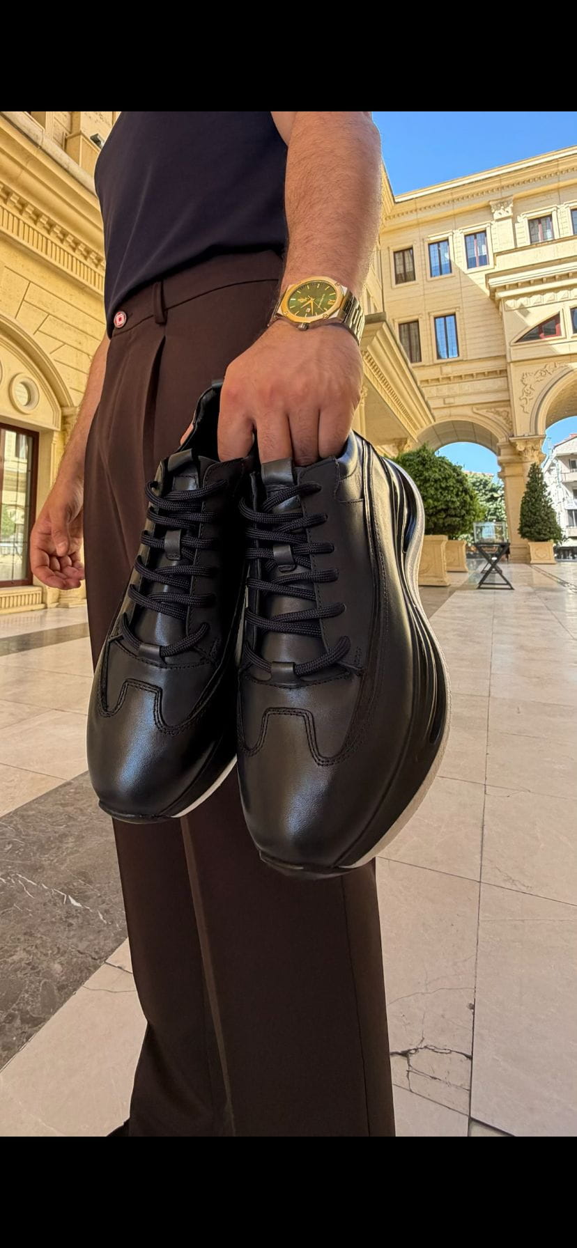 Lifestyle side view of Torino black leather runner sneaker in an outdoor architectural setting.