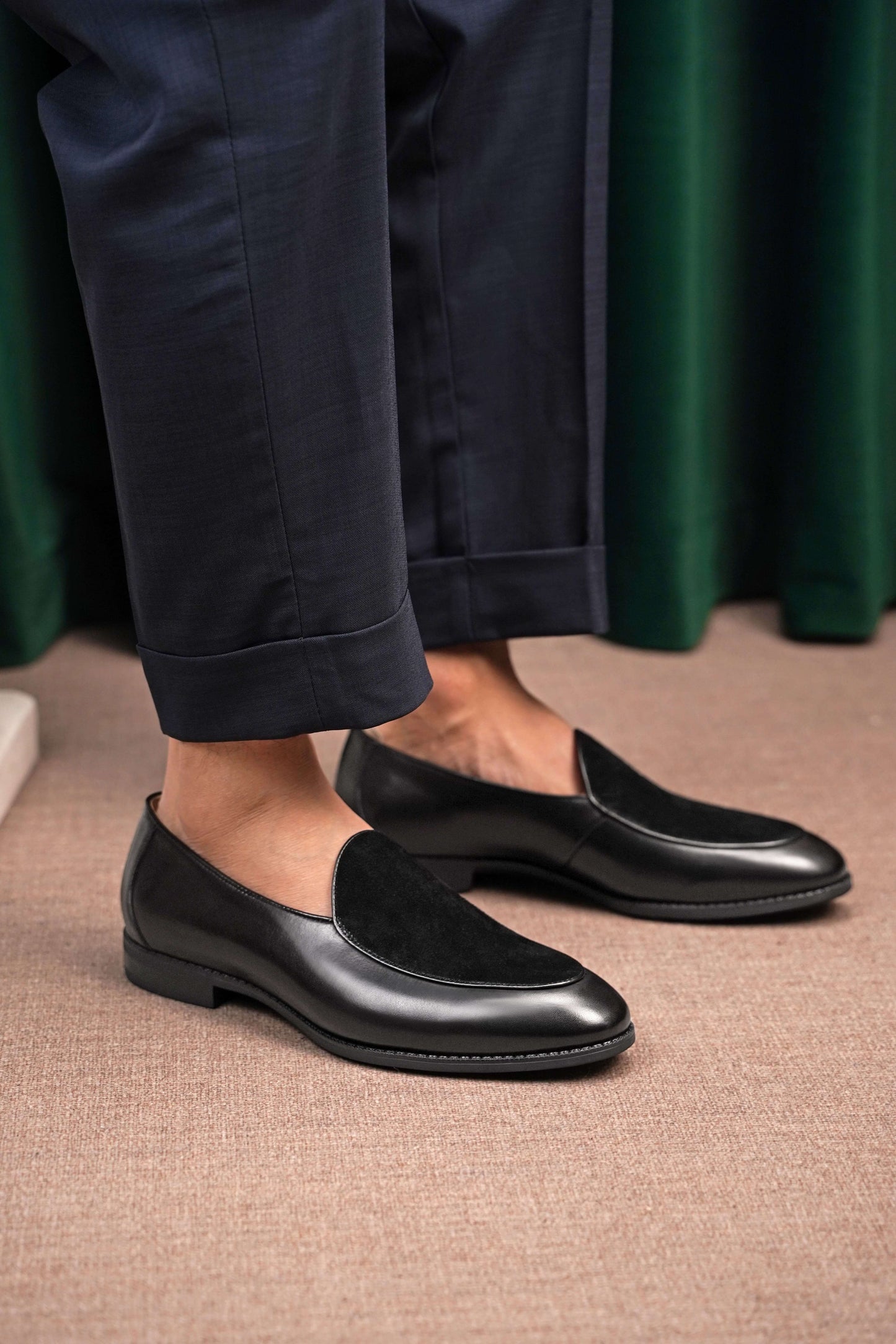 Velvet Crest Black Leather Suede Loafers – worn by a man in navy trousers, standing on a patterned rug, highlighting the unique texture contrast and sleek profile.
