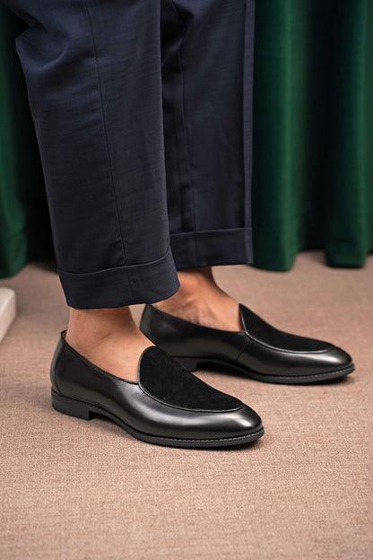 Velvet Crest Black Leather Suede Loafers – worn by a man in navy trousers, standing on a patterned rug, highlighting the unique texture contrast and sleek profile.