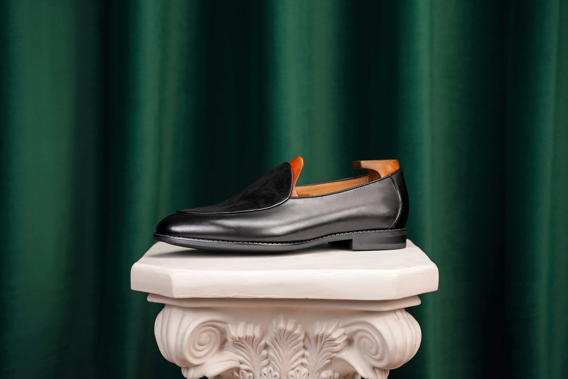 Velvet Crest Black Leather Suede Loafer – side view with shoe tree, resting on a white classical pedestal, highlighting the contrast in textures for refined ease.