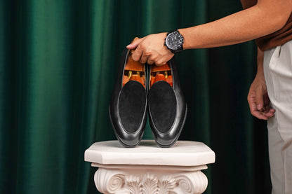 Velvet Crest Black Leather Suede Loafers – pair held by a man's hand with a watch, showcasing the contrast between the black leather and suede, for effortless style.