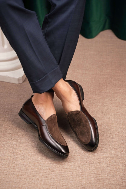 Velvet Crest Brown Leather Suede Loafers – worn by a man in navy trousers, standing on a patterned rug, highlighting the unique texture and effortless style.