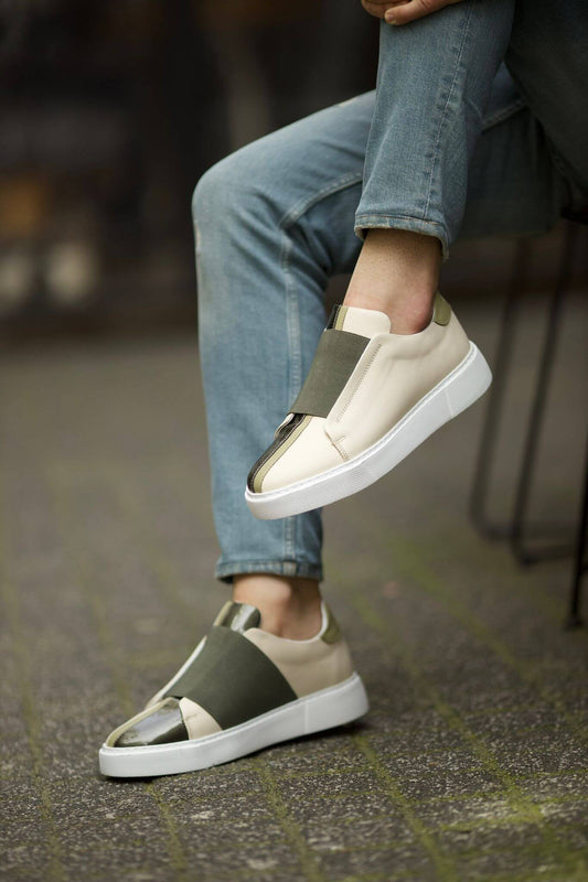 Vince Beige & Green Slip-On Sneakers - Sophisticated Comfort for Every Occasion – a man sitting in blue jeans, with one foot elevated, highlighting the two-tone leather and slip-on style.