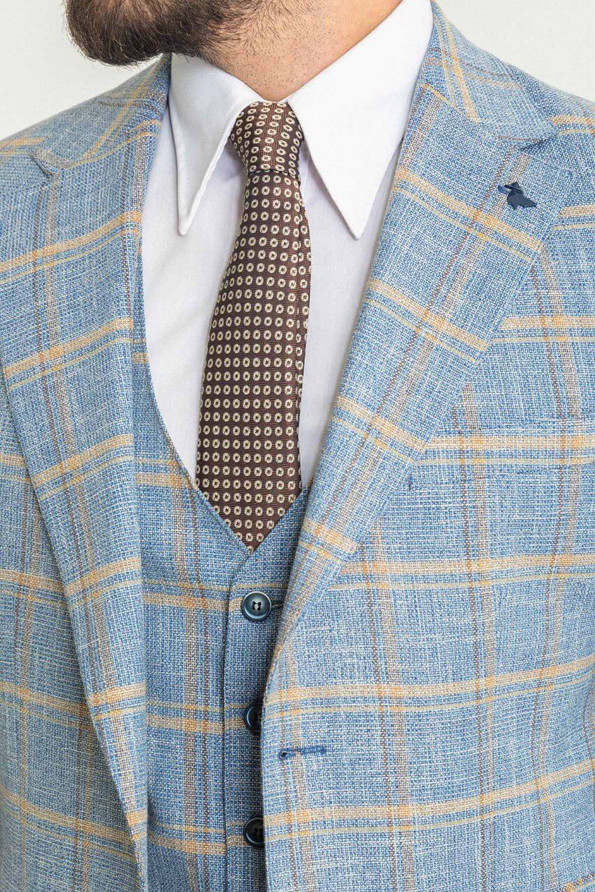 A stylish man wearing a Blue Checkered Three-Piece Suit stands confidently in a studio setting. The suit features a light blue color with a yellow checkered pattern, paired with a white dress shirt and a brown patterned tie, adding a touch of contrast and sophistication. Brown leather dress shoes complete the ensemble, enhancing the outfit's classic and elegant look. The man has neatly groomed hair and a trimmed beard, exuding a polished and refined appearance ideal for formal occasions.